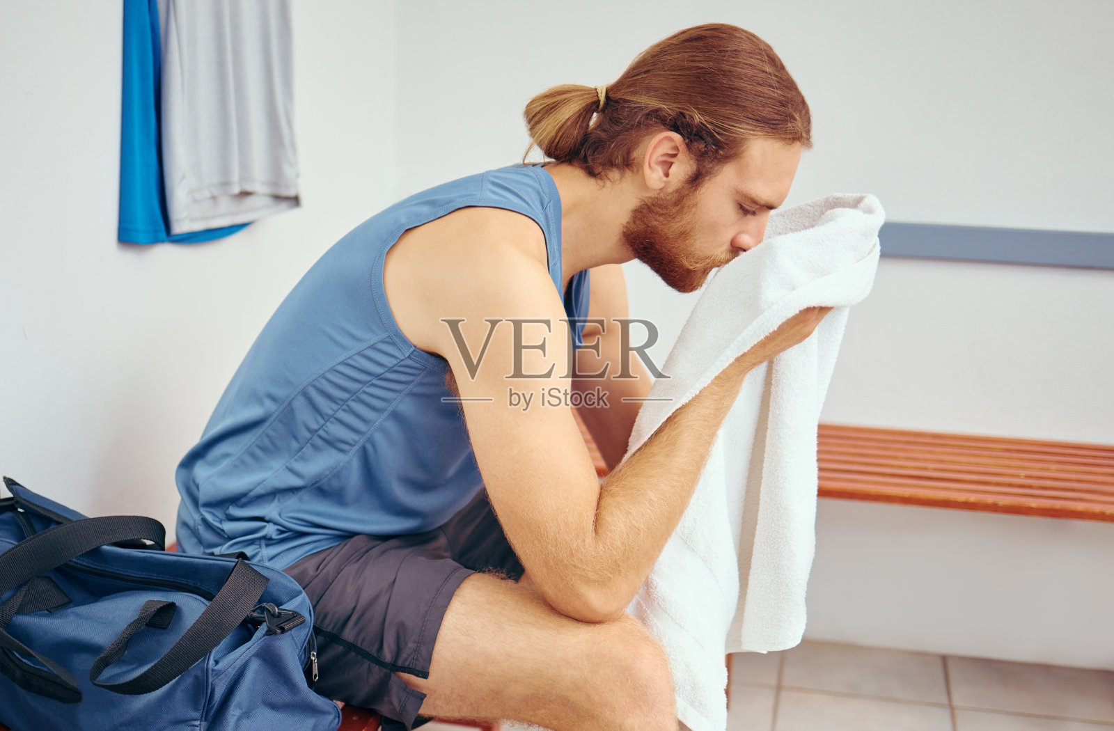 用毛巾擦脸的白人运动员。疲惫的年轻球员在壁球比赛后擦脸。职业运动员在健身房更衣室休息,暂停壁球比赛照片摄影图片