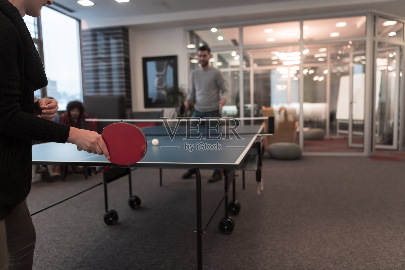 两个年轻的创业企业家在现代创意办公空间打乒乓球,背景是开会和头脑风暴照片摄影图片