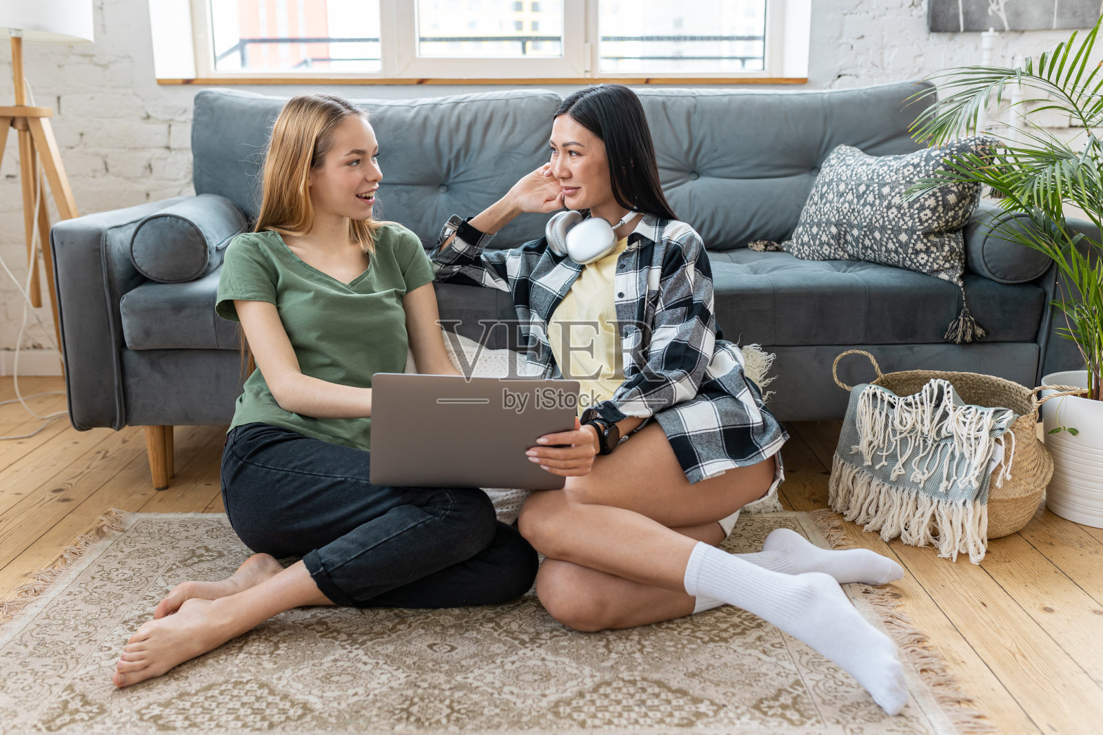 两个千禧一代的多元化女性朋友在家里看电影,上网浏览,购物,一起度过快乐的时光,聊天,聊天。女性使用的技术。亚洲和高加索模式。照片摄影图片