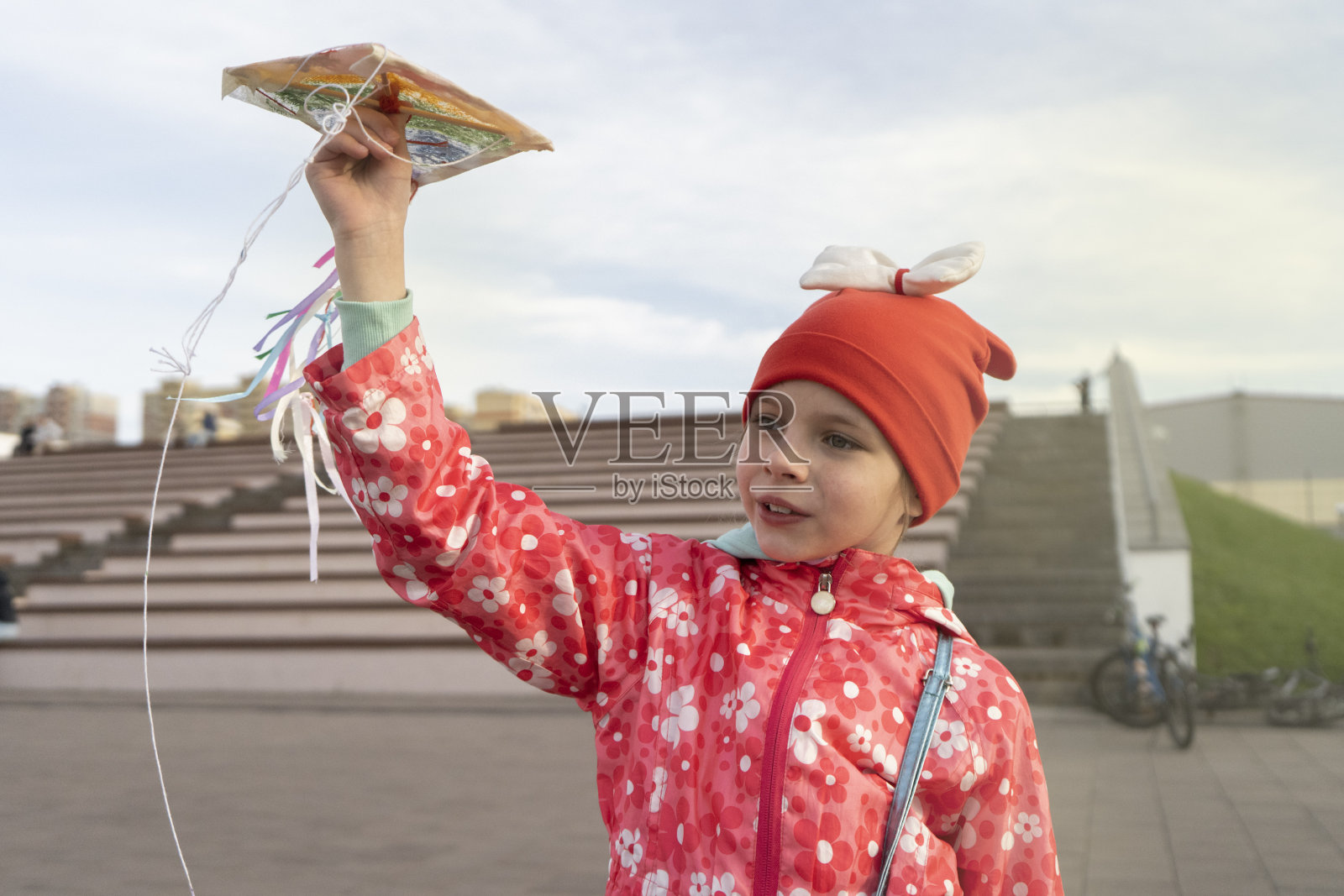 阳光明媚的天气里,一个戴着红色帽子和夹克的7岁女孩在空地上放风筝照片摄影图片