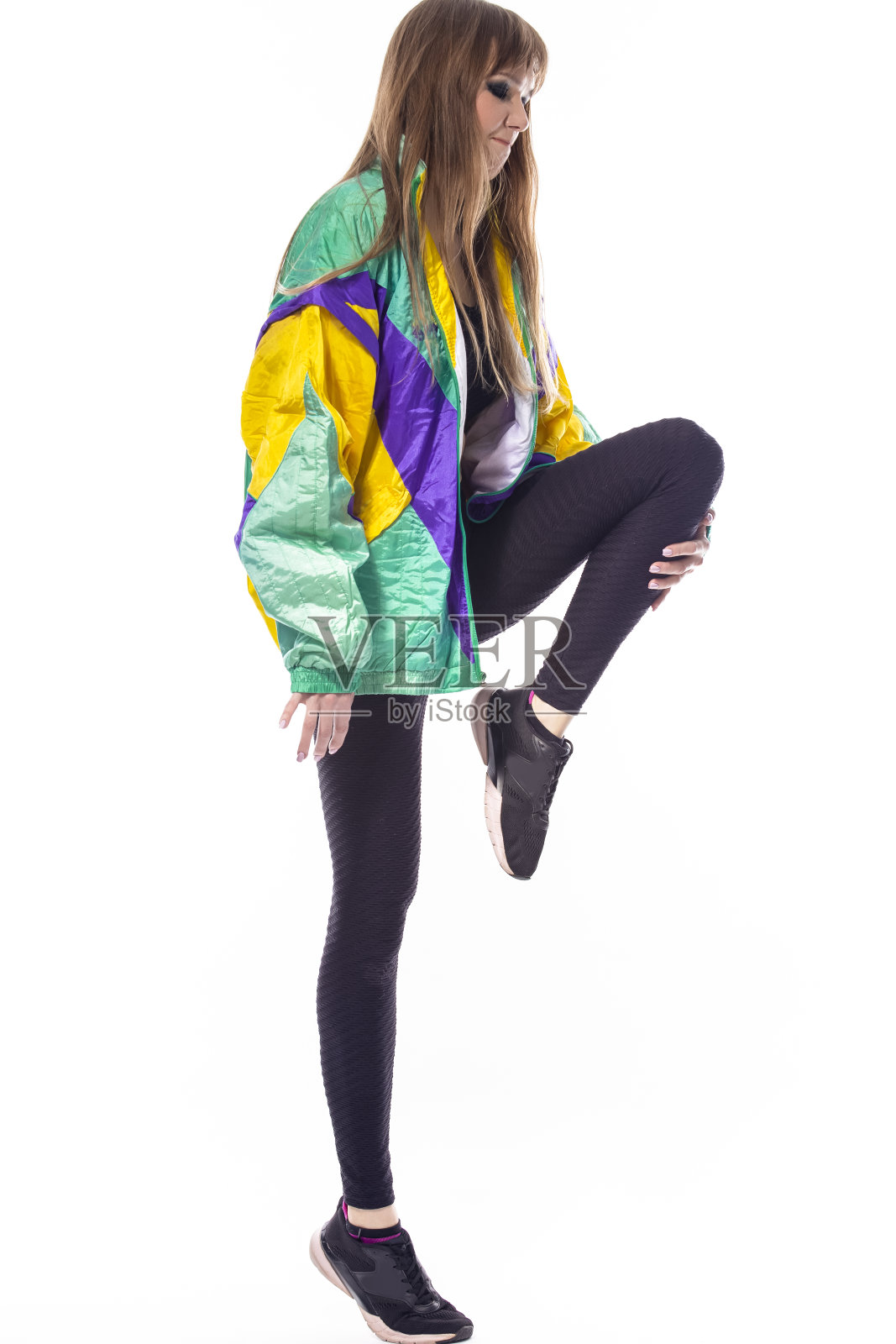 全身肖像积极迷人的白人女运动员运动员在健身紧身服装穿彩色防风夹克,而抬高腿在白色。照片摄影图片