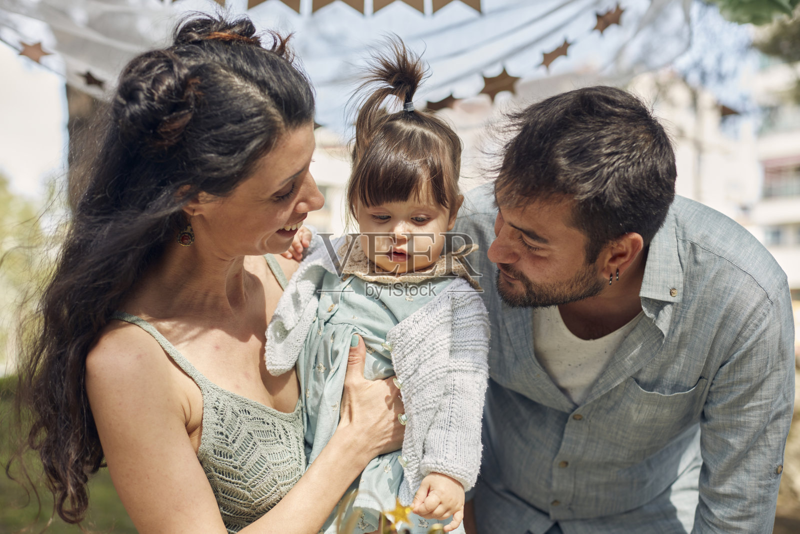 在花园里为小女儿庆祝生日,爸爸妈妈一起吹生日蛋糕。照片摄影图片