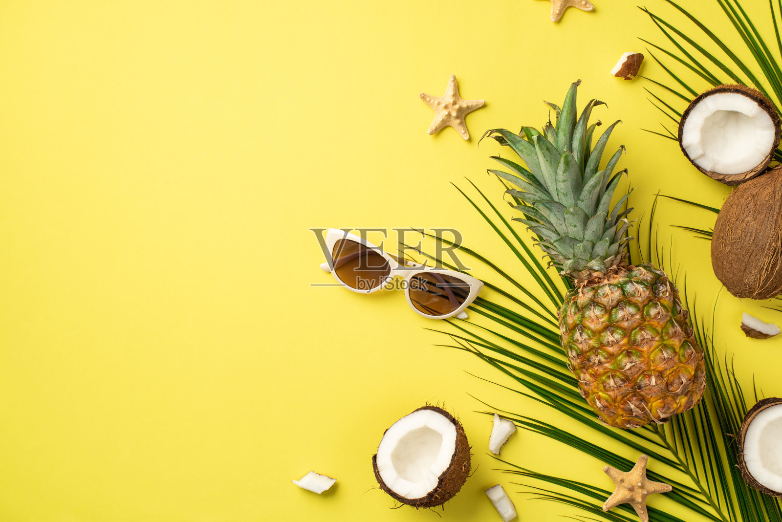 暑假的概念。顶视图照片的新鲜热带水果椰子菠萝太阳镜海星和棕榈叶孤立的黄色背景与copyspace照片摄影图片