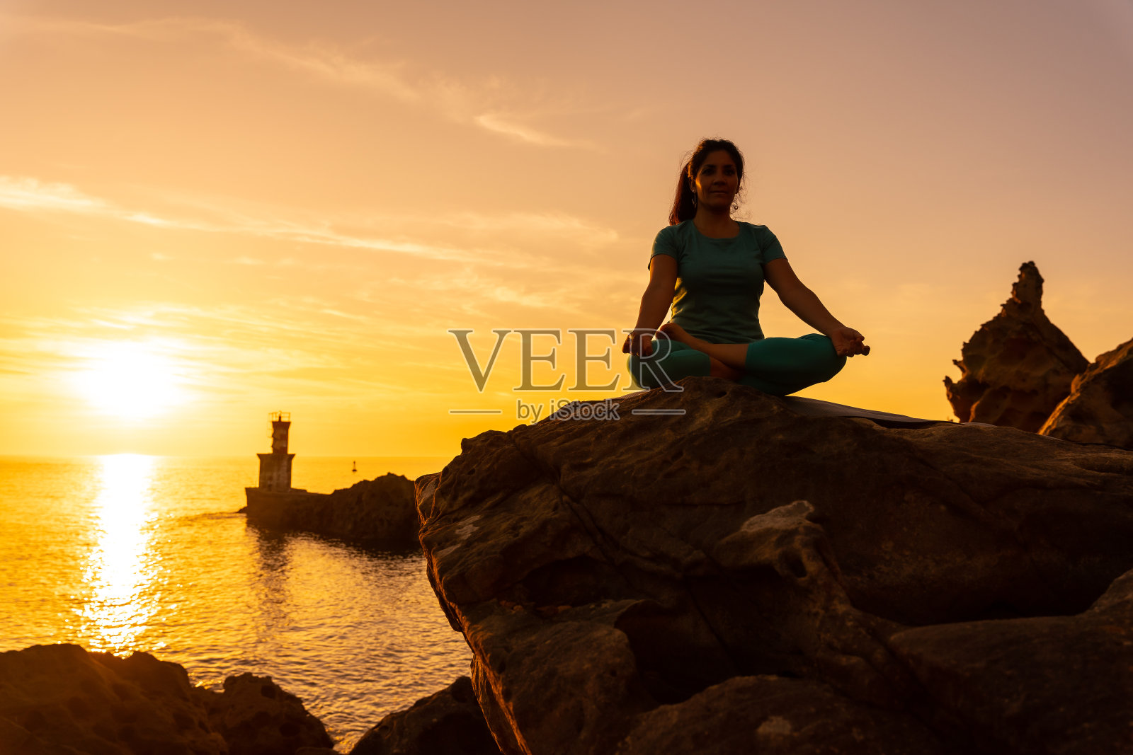 日落时分,在海上灯塔旁做冥想和瑜伽练习的女人,健康和的生活,户外普拉提,莲花生照片摄影图片