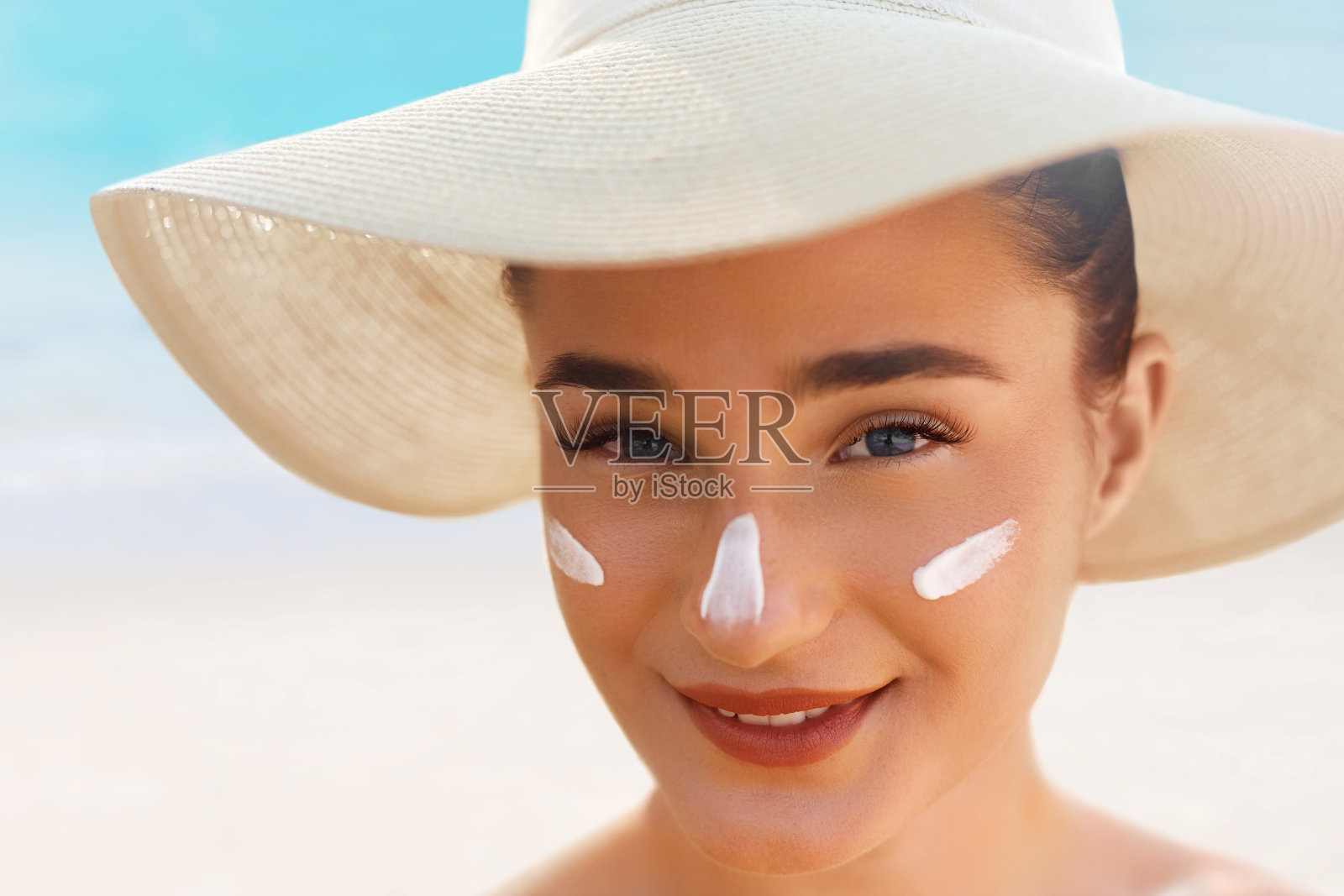 脸上涂抹防晒霜的年轻女子,戴着帽子在皮肤上涂抹保湿乳液,呵护肌肤,防晒照片摄影图片