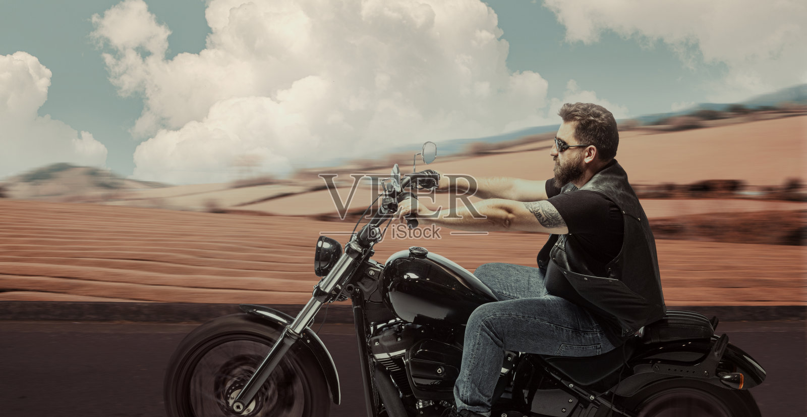 时尚野蛮的摩托车手骑摩托车在高速公路在夏天的晚上时间。复古的电影背景和戏剧性的多云天空。时尚概念、风格和爱好照片摄影图片