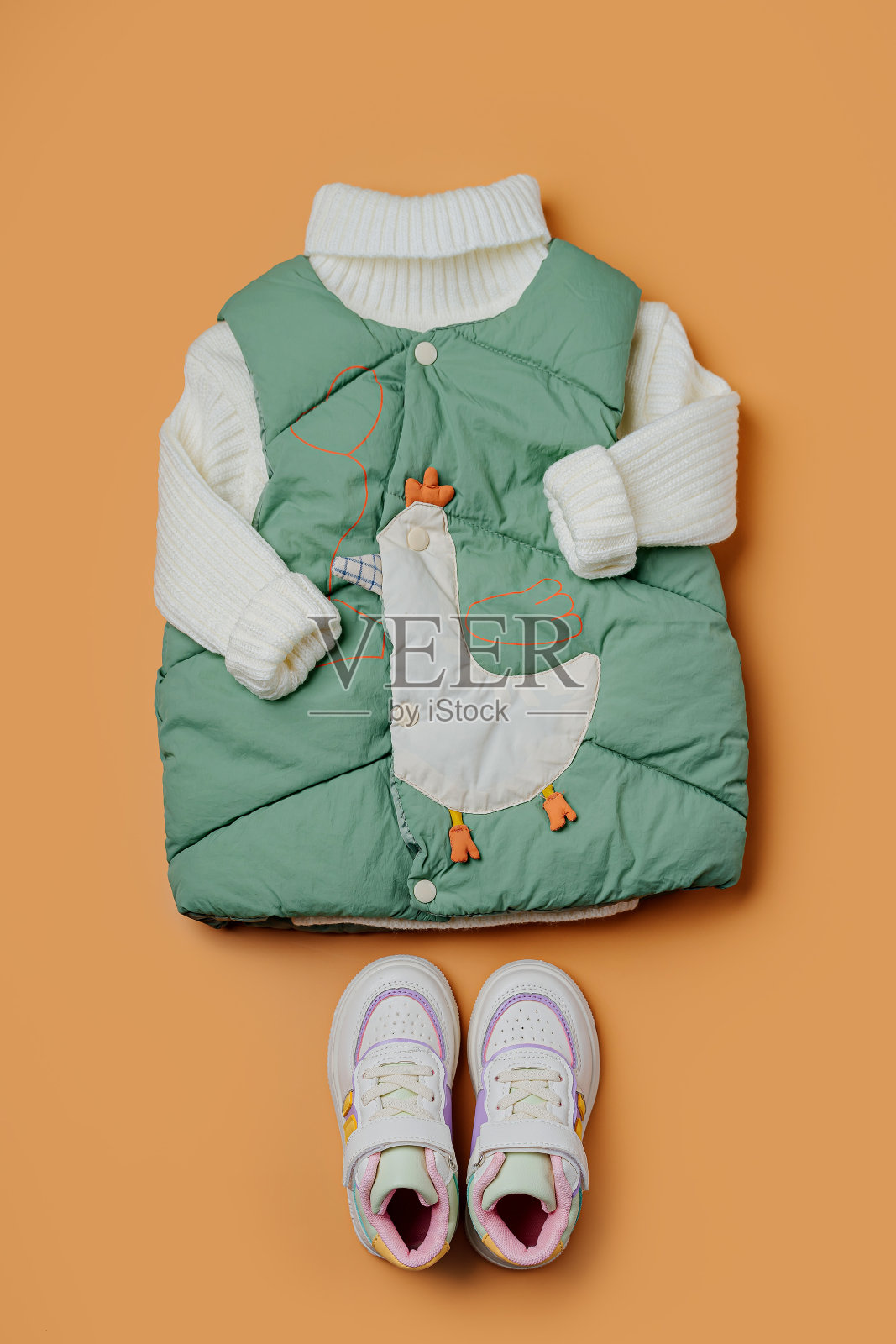 绿色马甲与温暖的毛衣在橙色的背景。时尚儿童外套。冬季时尚服装照片摄影图片