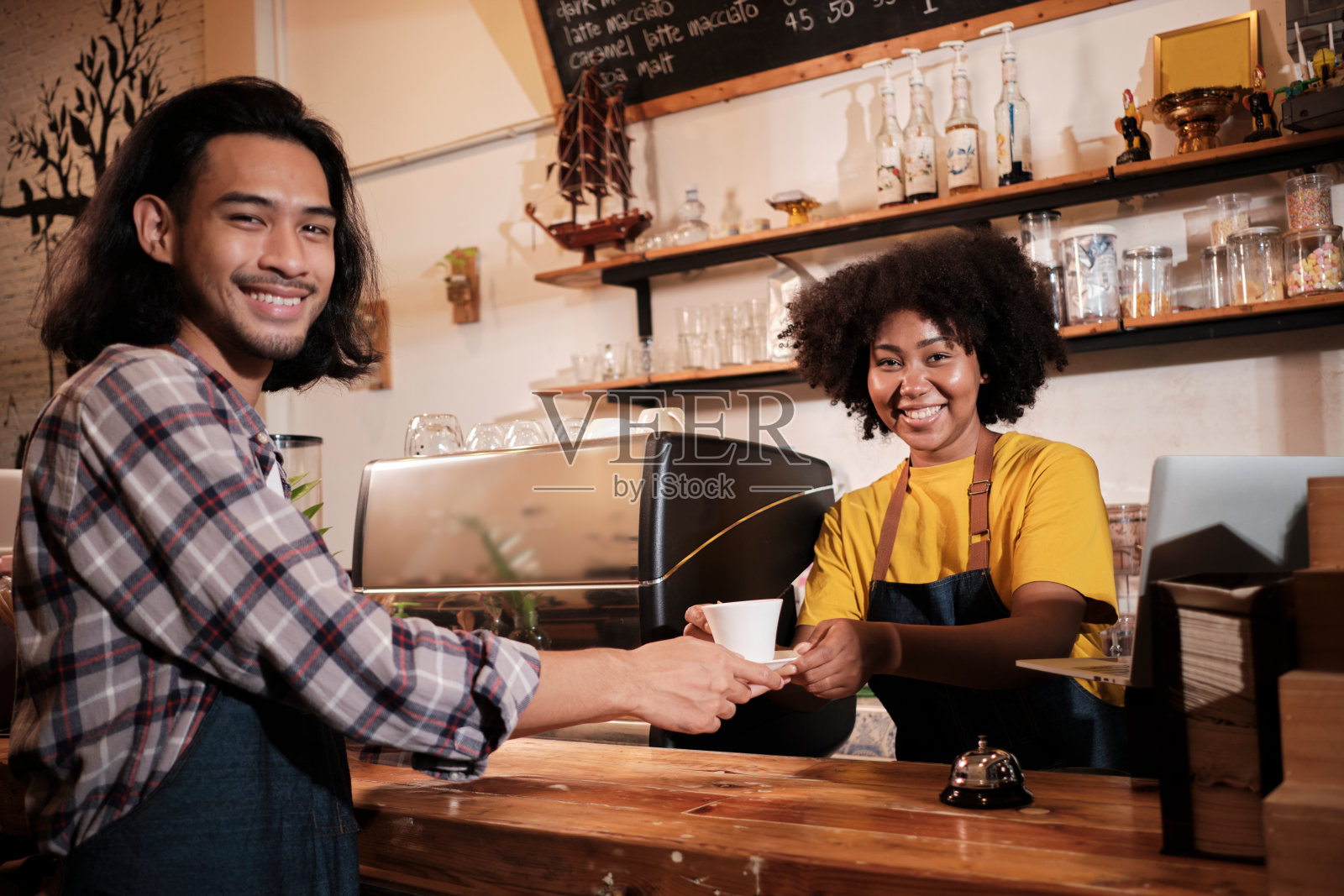 两名咖啡师搭档在咖啡店的柜台上工作,脸上洋溢着愉快的笑容。照片摄影图片