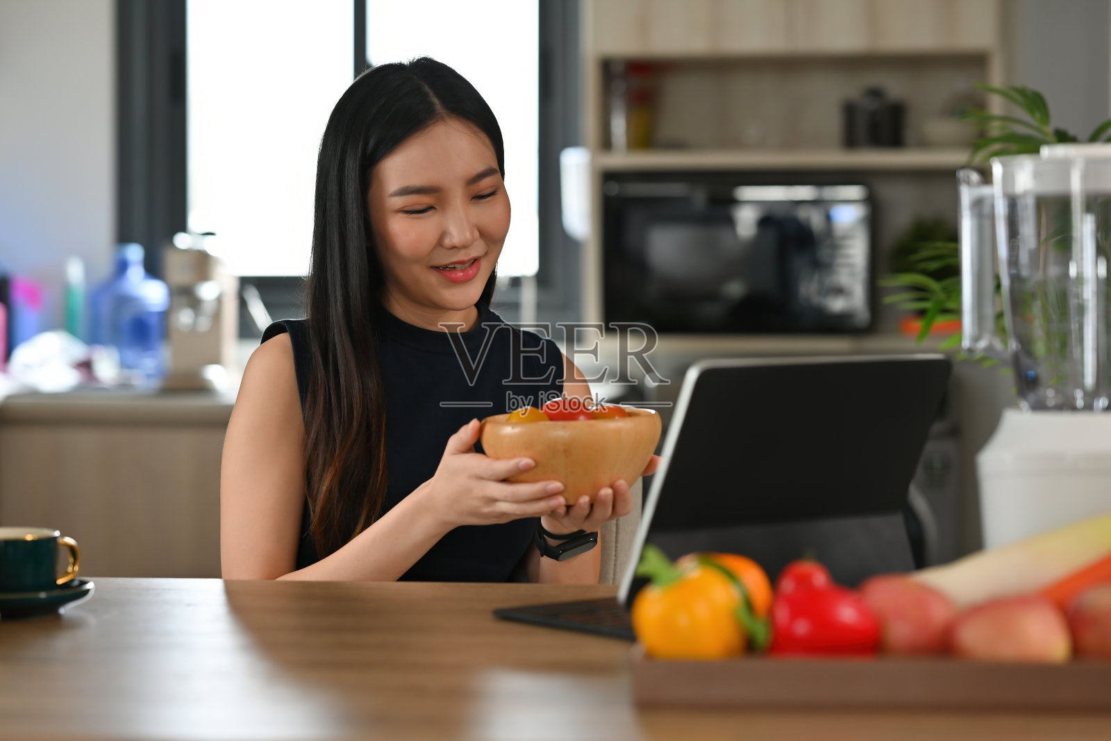 一个年轻漂亮的亚洲女人的肖像,拿着一碗蔬菜,有一个平板看食谱,食物,健康和烹饪的概念。照片摄影图片