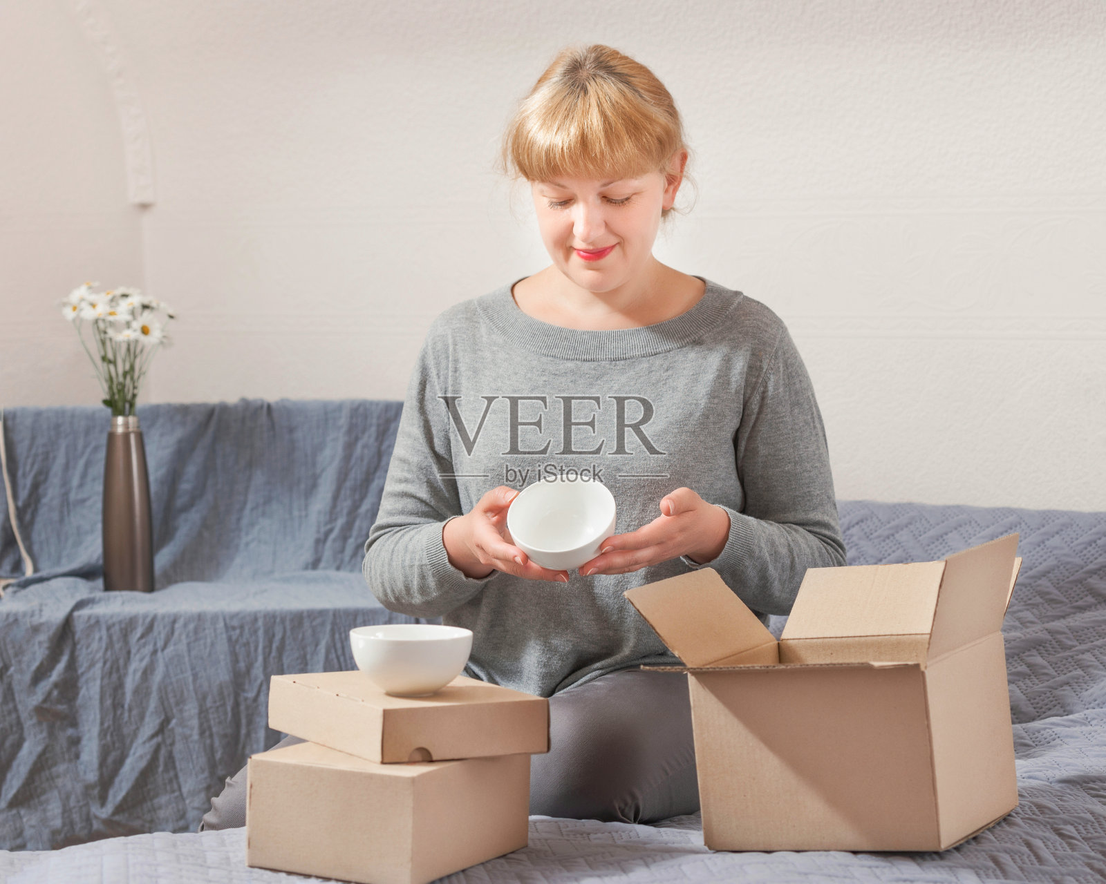 一位满意的女购物者在网上商店通过邮政快递收到了一件商品,她坐在沙发上打开包裹并查看货物。照片摄影图片
