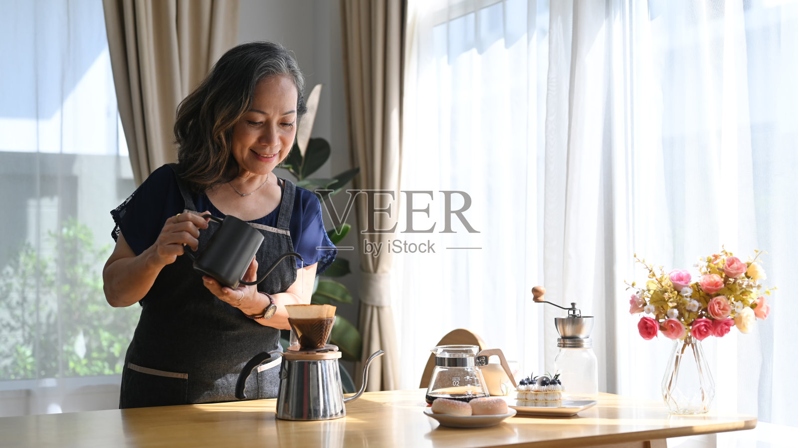 积极的中年人站在厨房的桌子上,煮着滴滤咖啡,享受着她的早晨。照片摄影图片