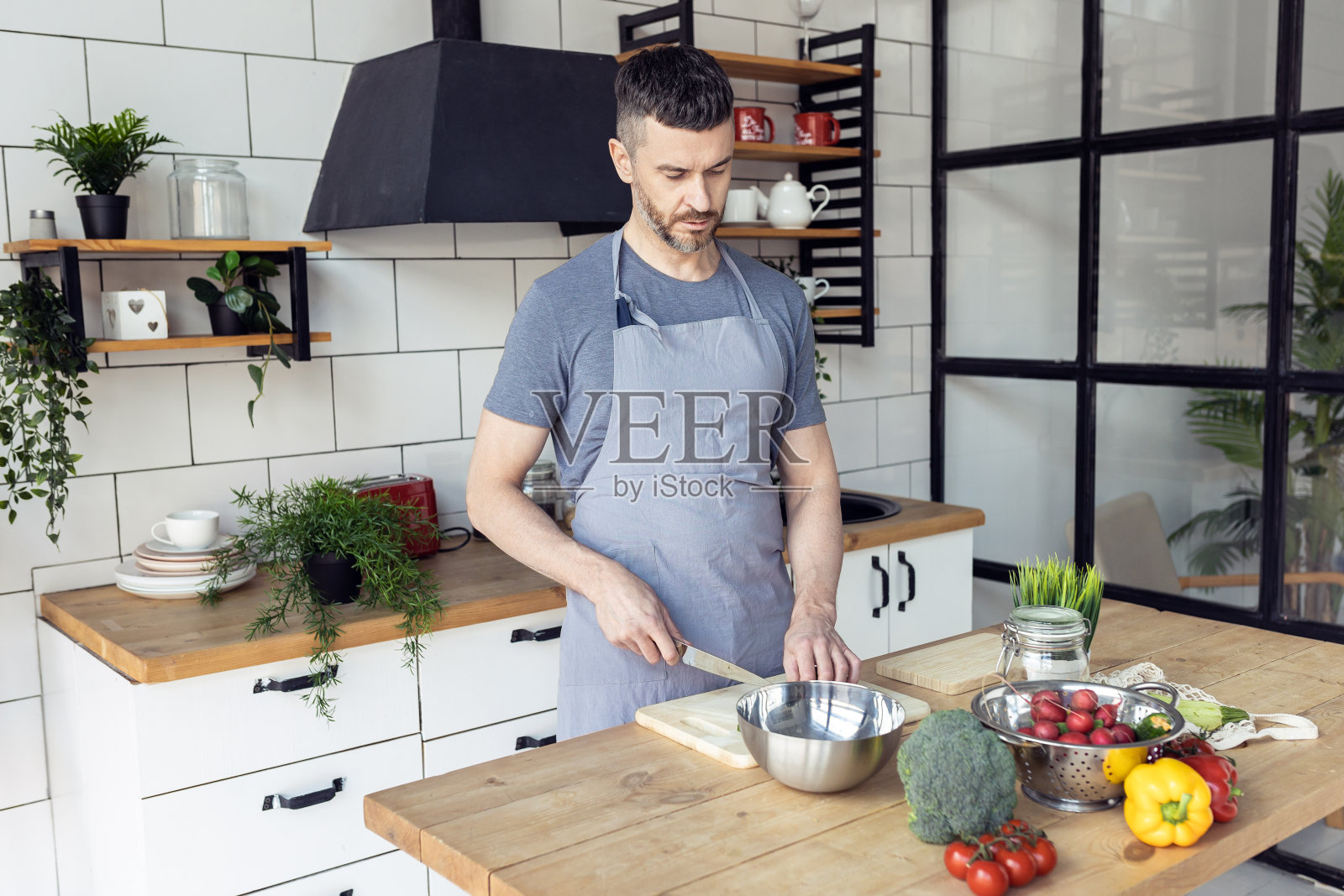 英俊的父亲,强壮的年轻人用新鲜的有机食材烹饪健康的蔬菜沙拉,在家里的厨房里美味的食物。男人做家务。成熟的辣椒,番茄,黄瓜照片摄影图片