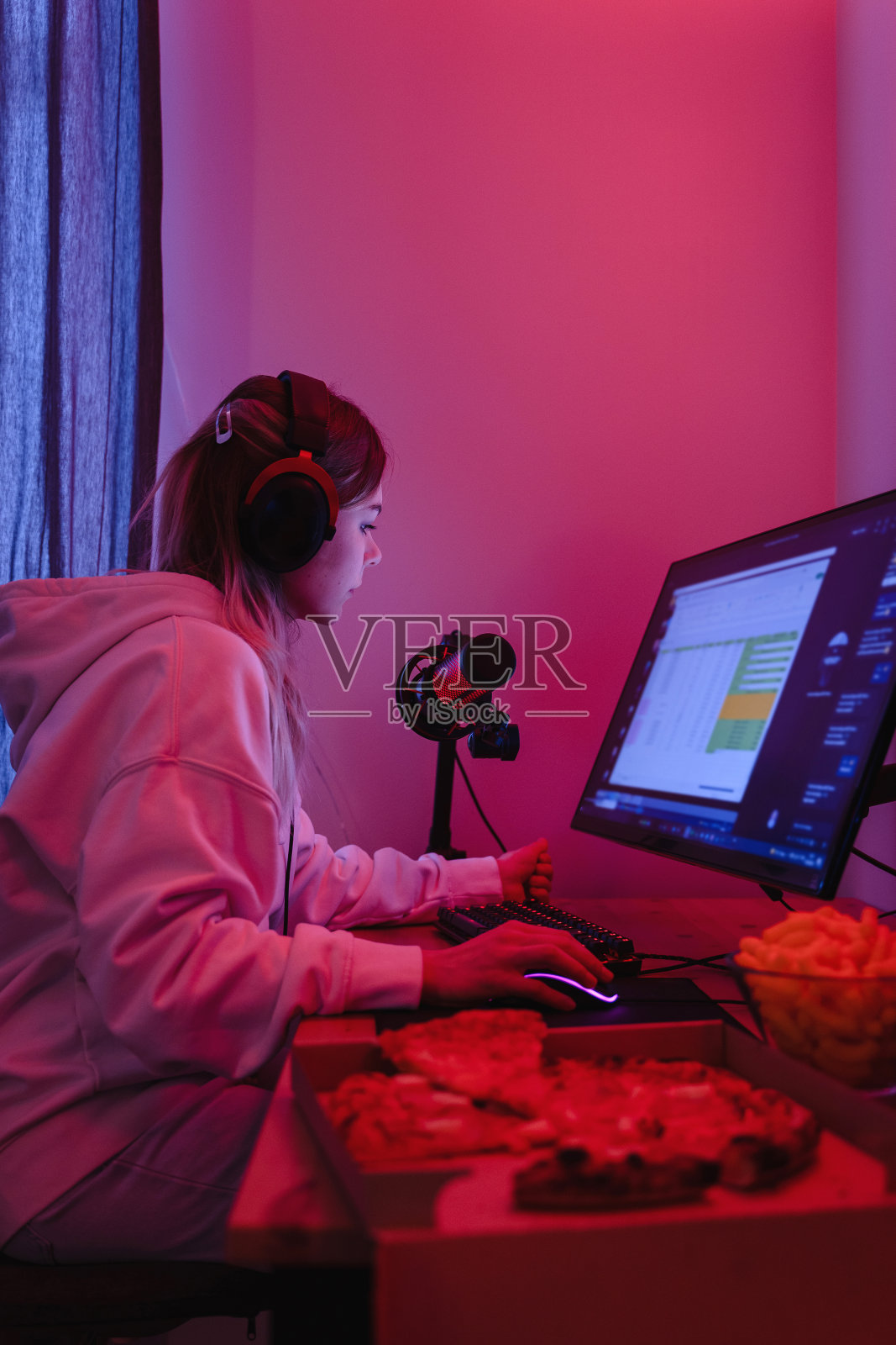 女性游戏玩家或软件开发人员晚上坐在有霓虹灯的房间里,坐在现代个人电脑前吃垃圾食品照片摄影图片