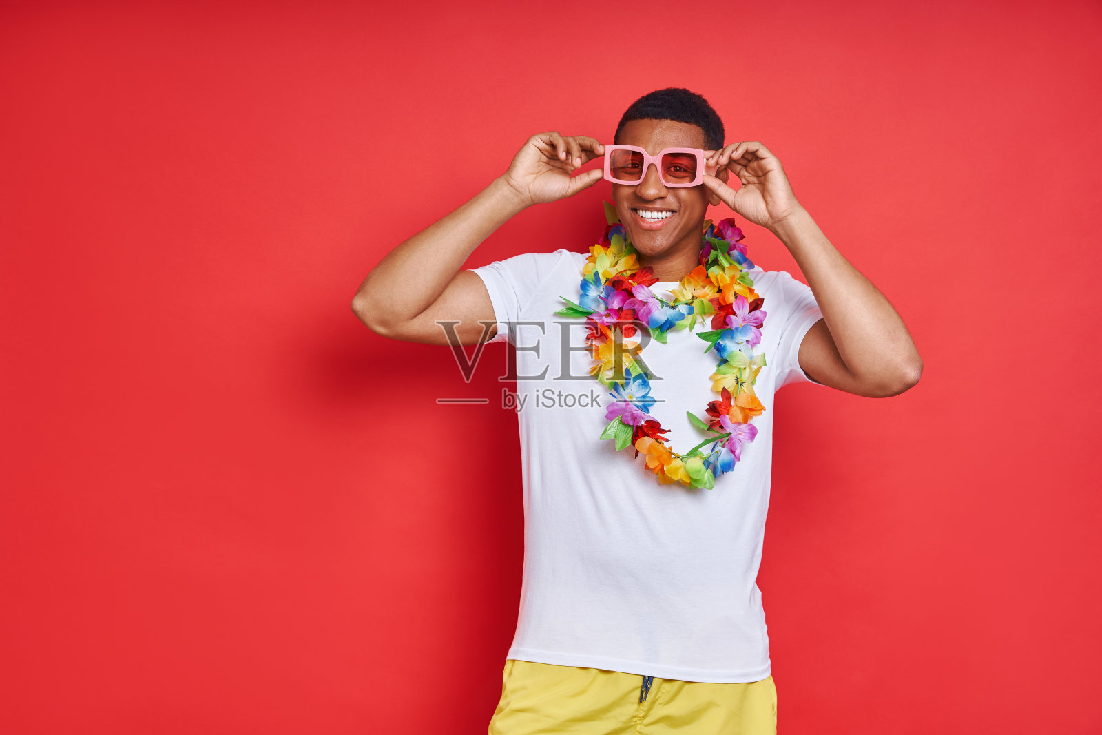 快乐的年轻人在夏威夷项链站在红色的背景照片摄影图片