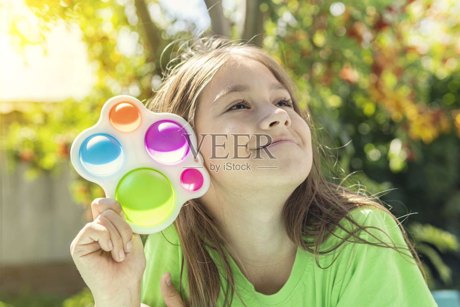 一个有趣的女孩躲在玩具后面。给小女孩画一个现代的娃娃玩具。五颜六色明亮的pop它玩具简单的酒窝。抗压力感官玩具烦躁推简单的酒窝照片摄影图片
