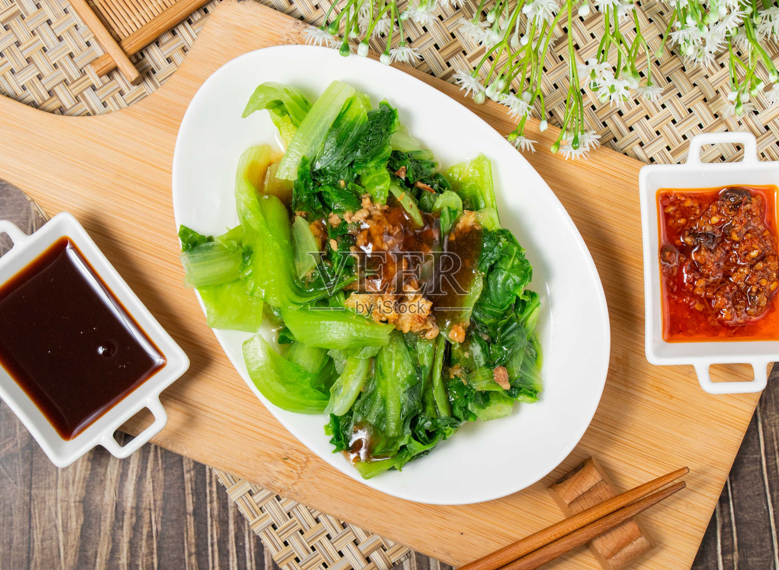 木制砧板上白色托盘中的焯水蔬菜和酱汁(顶视图)照片摄影图片