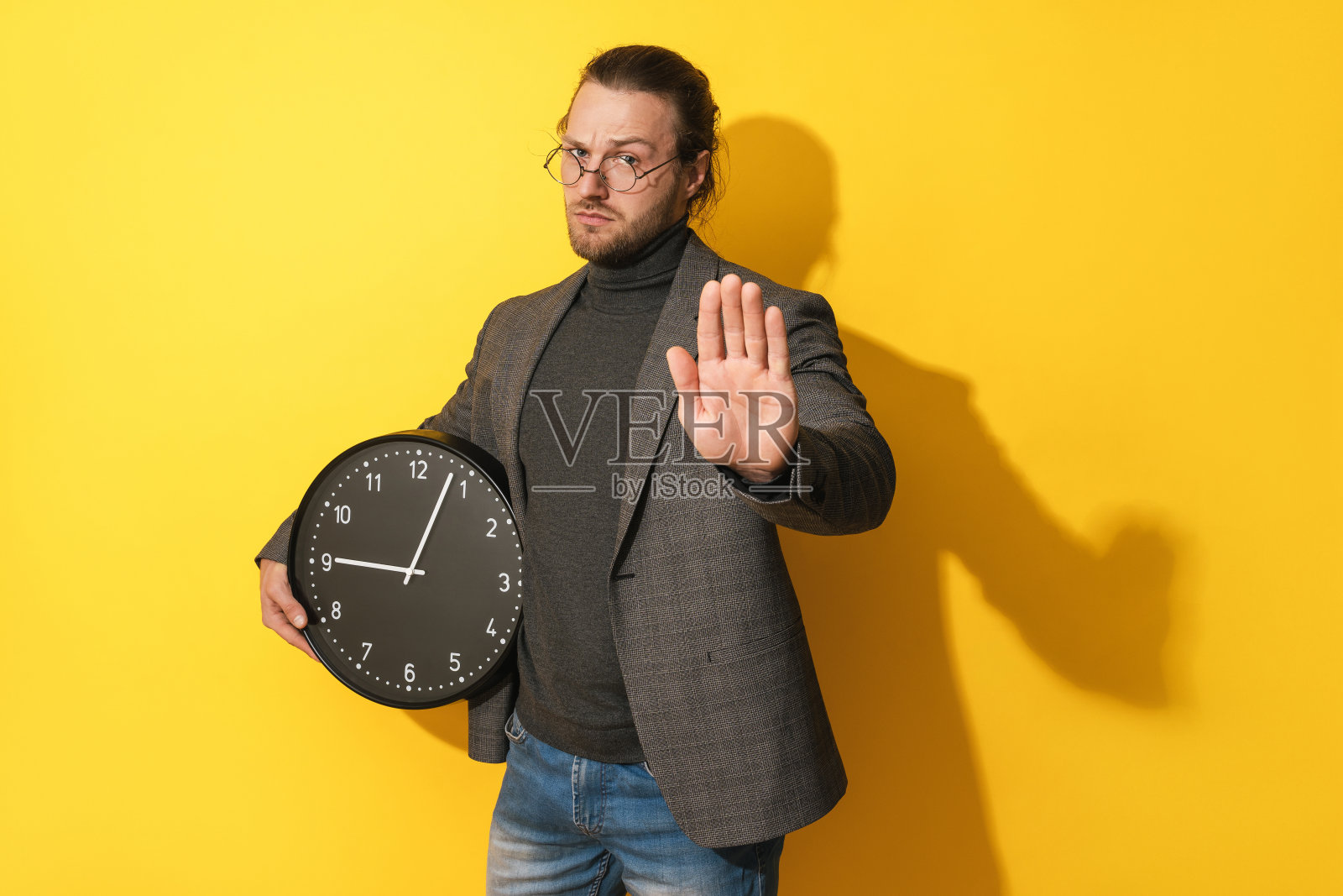 严肃的男人拿着钟,在黄色背景上显示停止的手势照片摄影图片