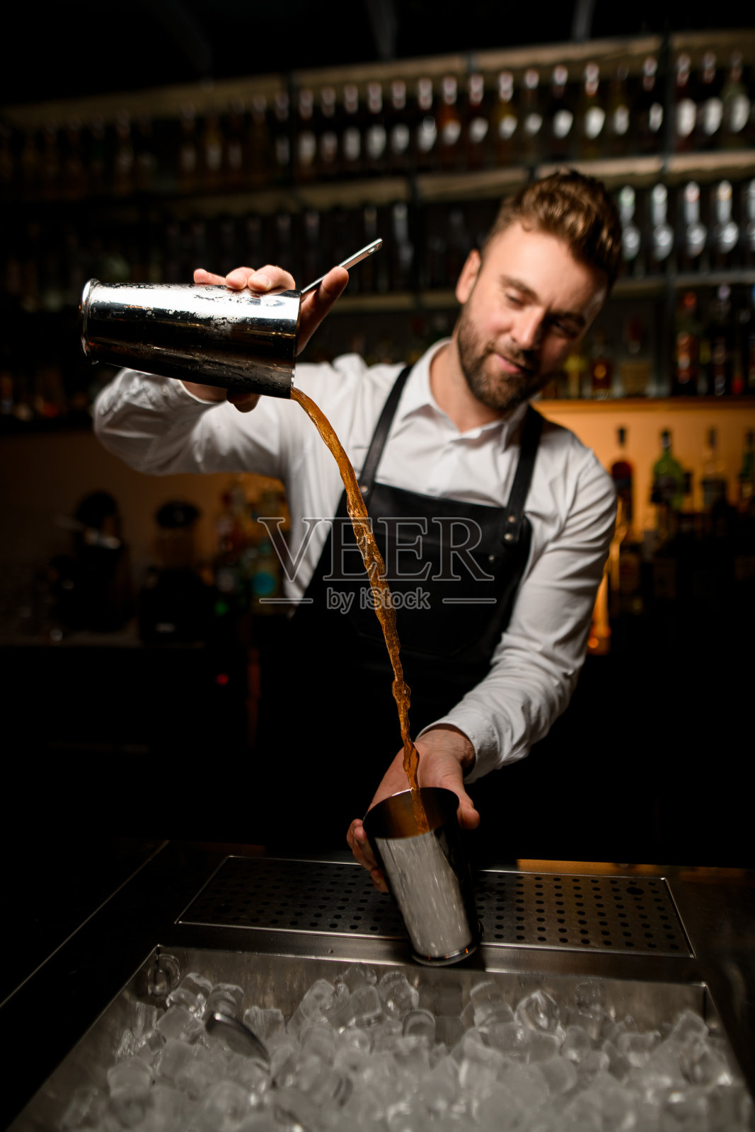 调酒师熟练地将鸡尾酒从一个摇杯倒入另一个摇杯。照片摄影图片