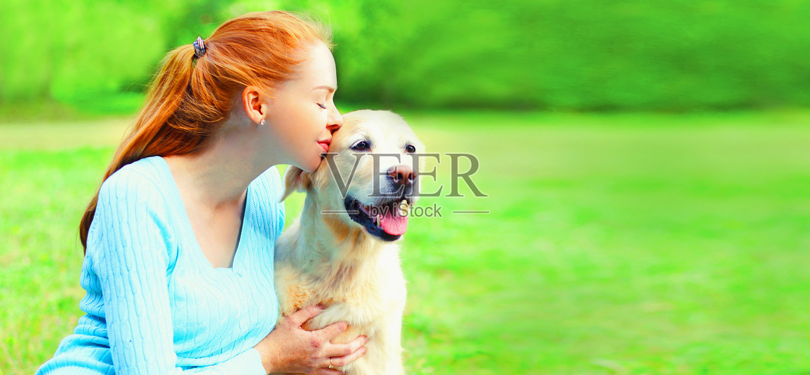 快乐的女人在夏天的公园里亲吻她的金毛猎犬照片摄影图片