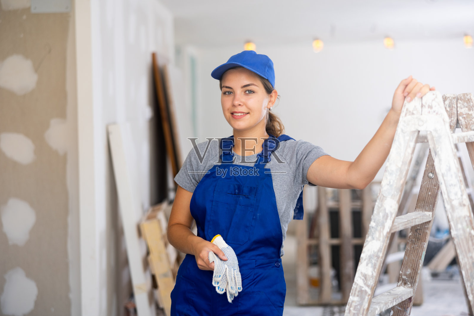 积极的建筑女工肖像,蓝色工作服旁边的梯子照片摄影图片