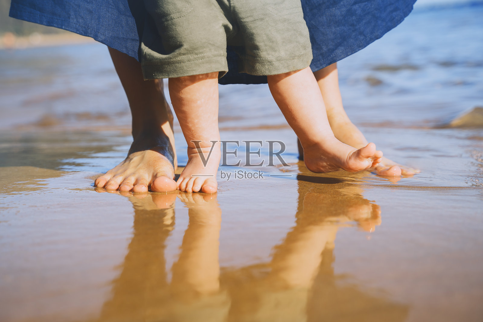 婴儿的第一步。母亲和小孩赤脚走在海边的沙滩上。自然是幸福的年轻家庭。妈妈和宝宝在海滩上玩耍。近距离人类的脚。照片摄影图片