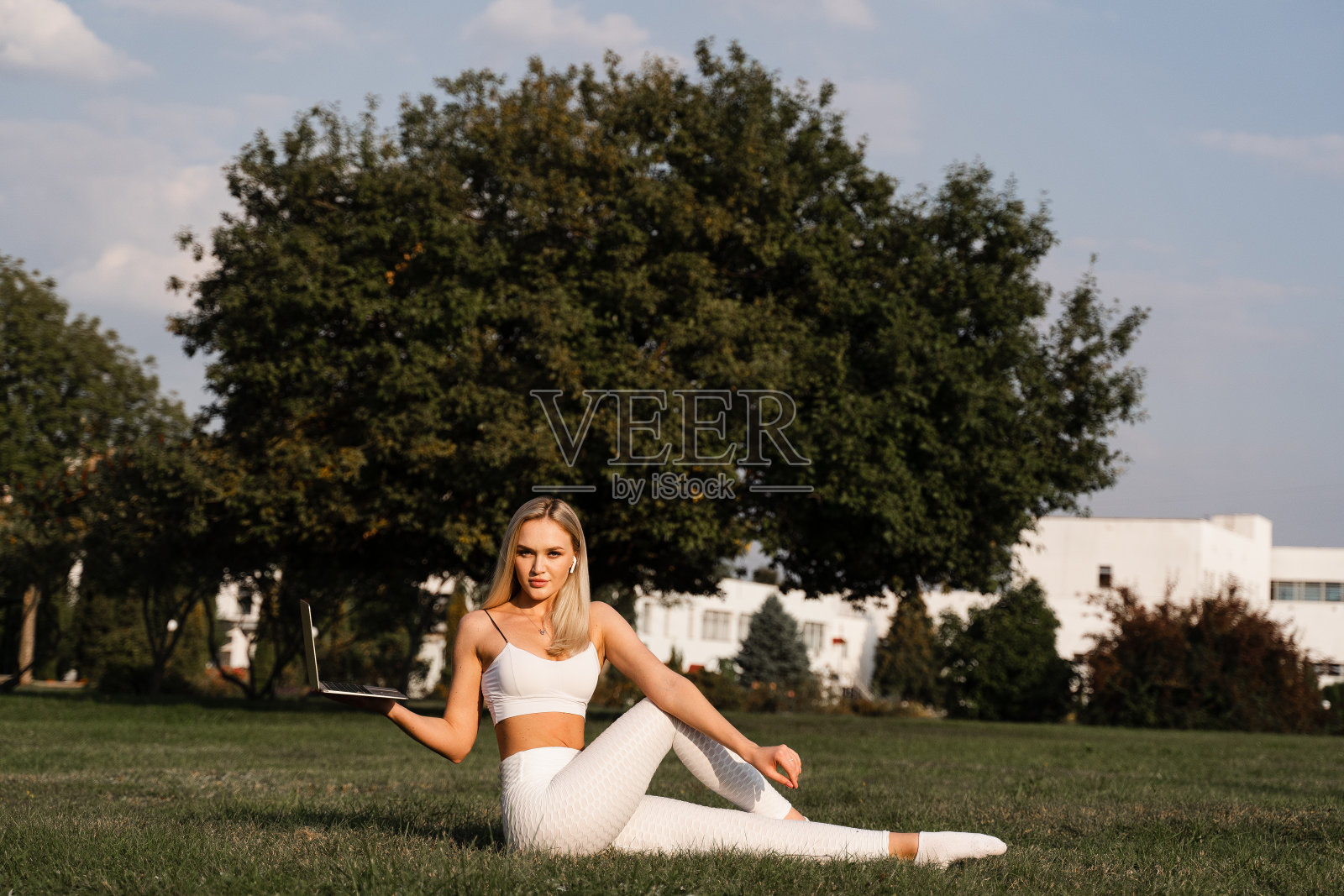 在公园里用笔记本电脑在线健身。适合金发在草地上和教练聊天。户外运动的生活方式。照片摄影图片