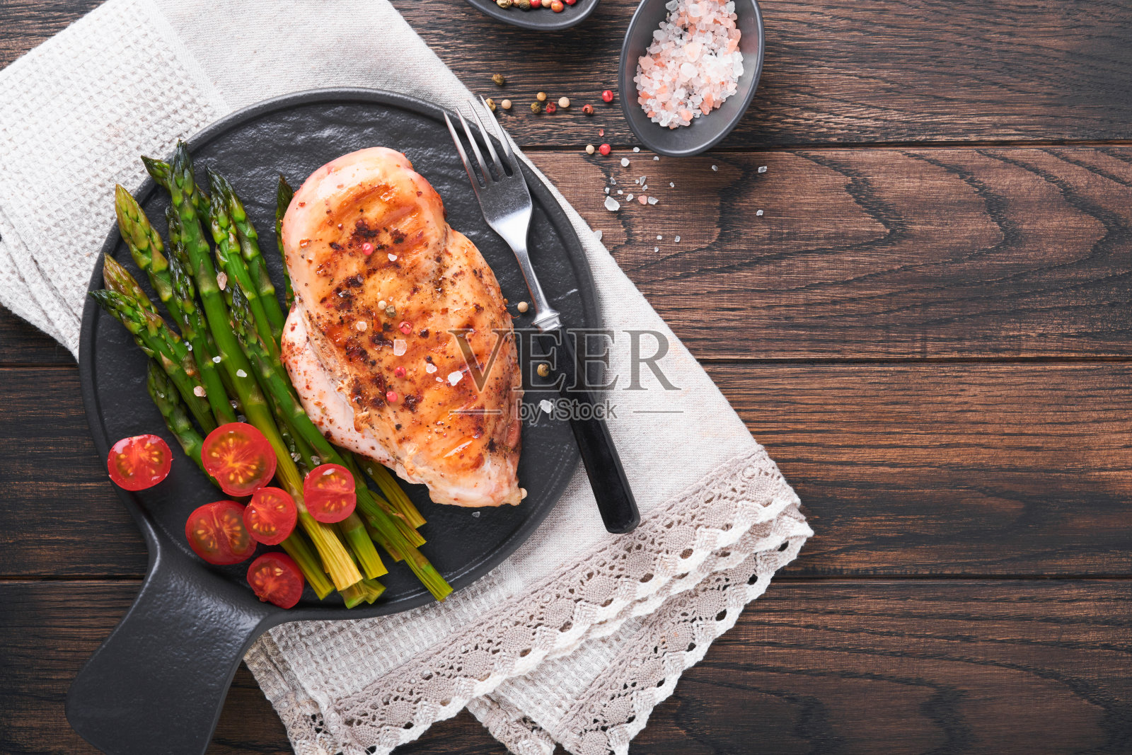 烤鸡胸肉配蔬菜。烤鸡排,芦笋和圣女果在黑色盘子上的木制黑暗的桌子背景。健康饮食的午餐。油炸烧烤牛排。前视图。照片摄影图片
