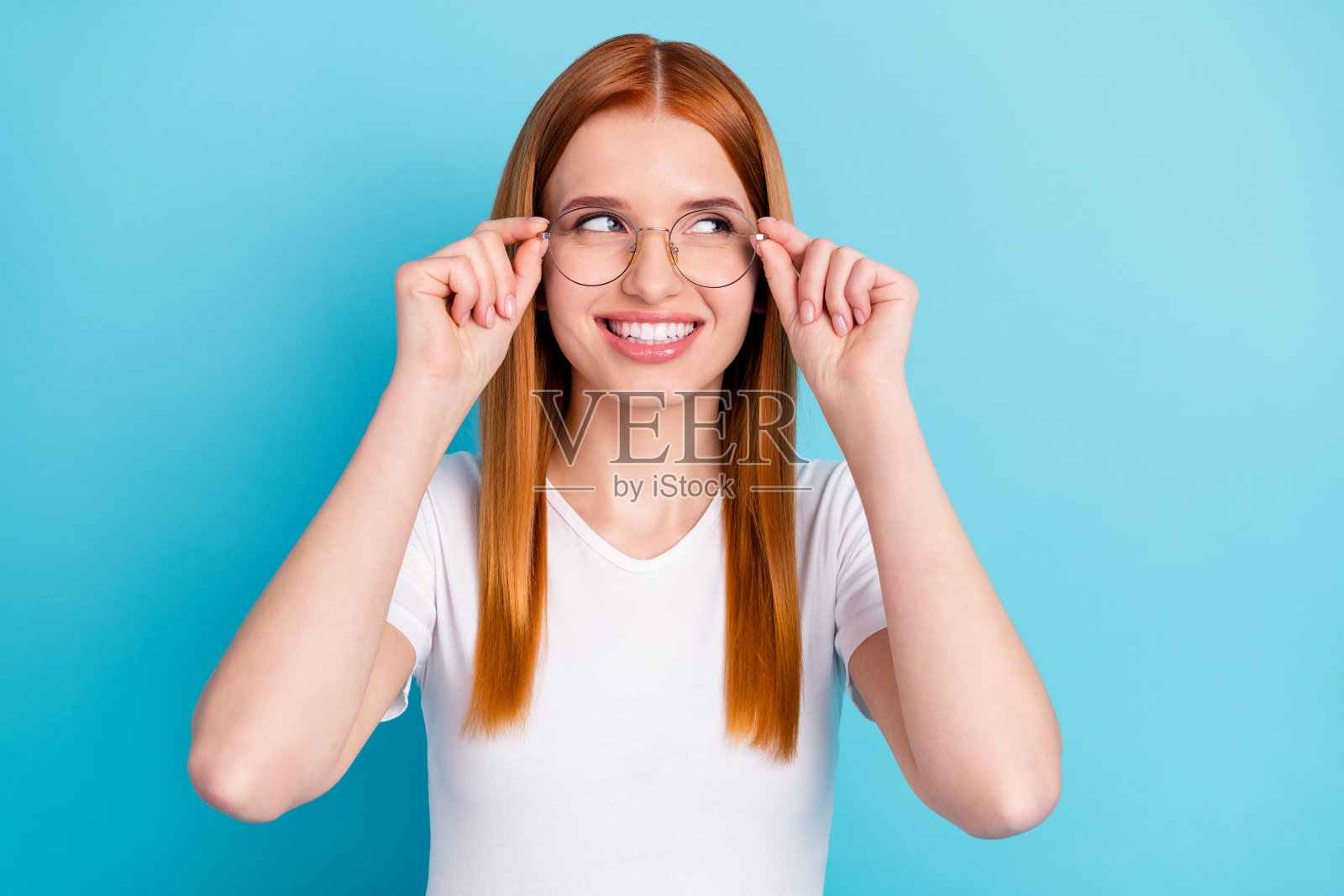 年轻迷人的女孩的照片快乐积极的微笑,手触摸眼镜看空的空间孤立在蓝色的背景照片摄影图片