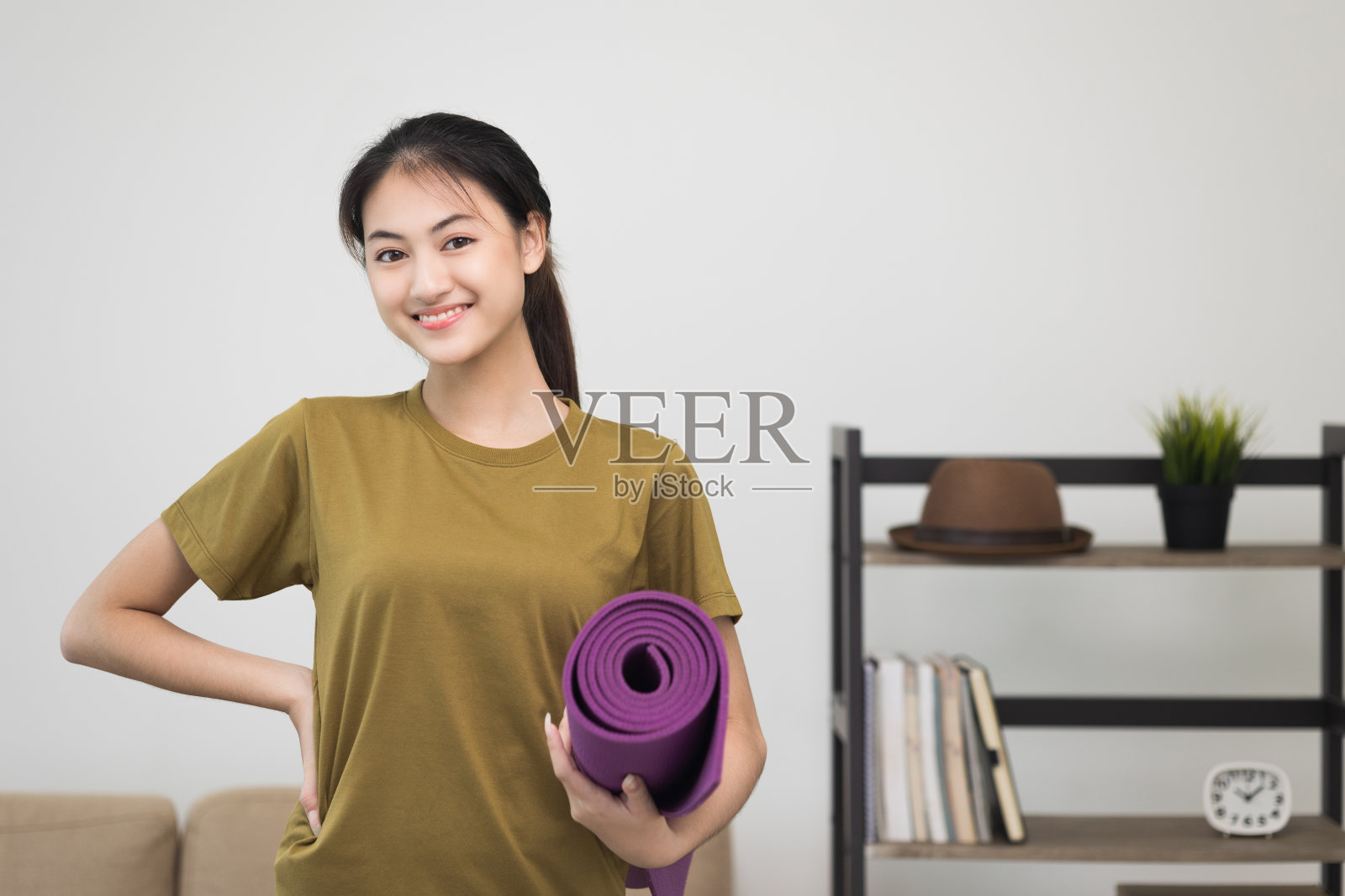 年轻美丽的亚洲女人站着姿势微笑的相机拿着瑜伽垫。愉快的运动女性锻炼和运动穿着运动服。迷人的女人在健身训练后放松。照片摄影图片