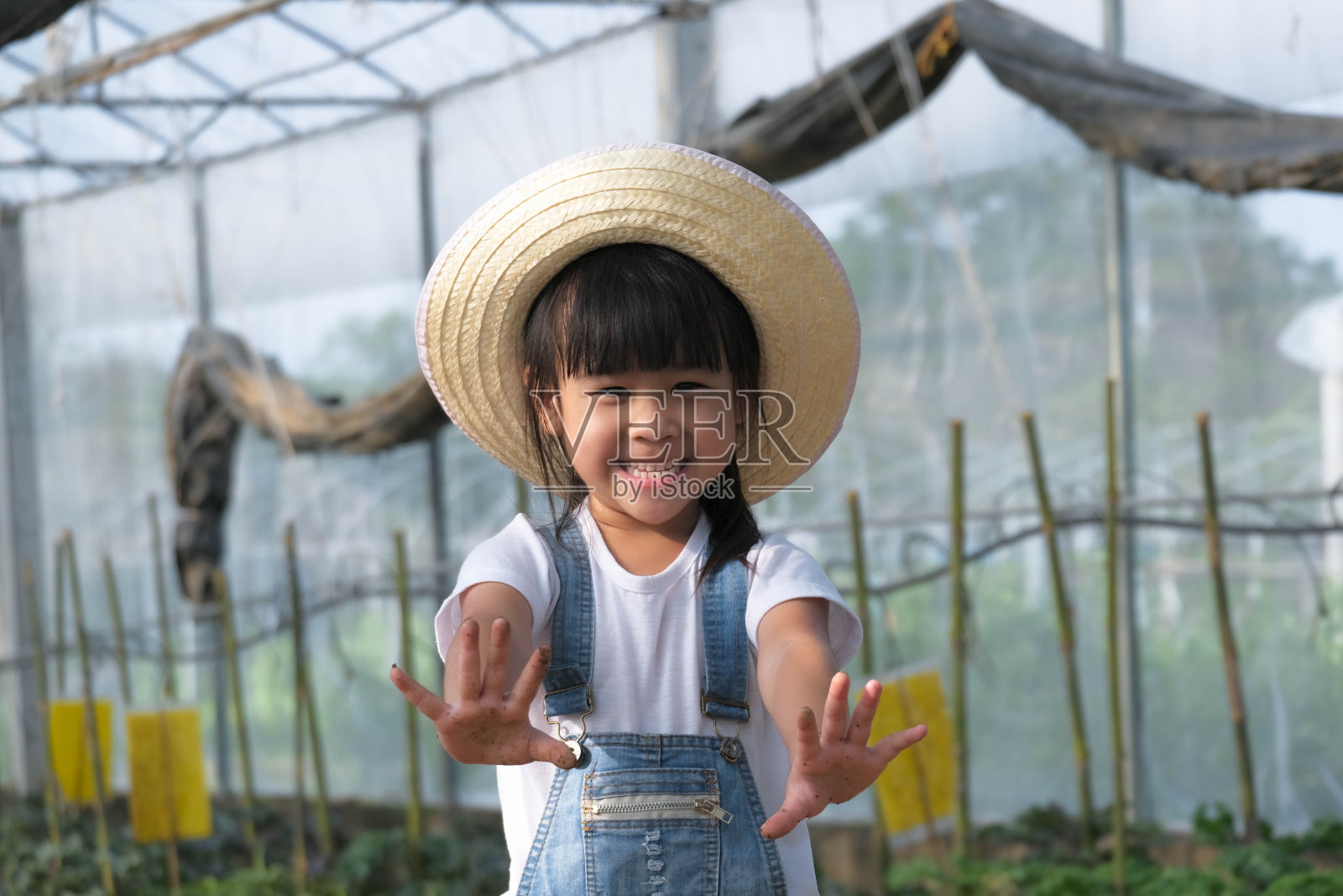 小女孩戴着帽子在花园里帮助她的妈妈,一个小园丁。可爱的女孩在菜园里玩。照片摄影图片