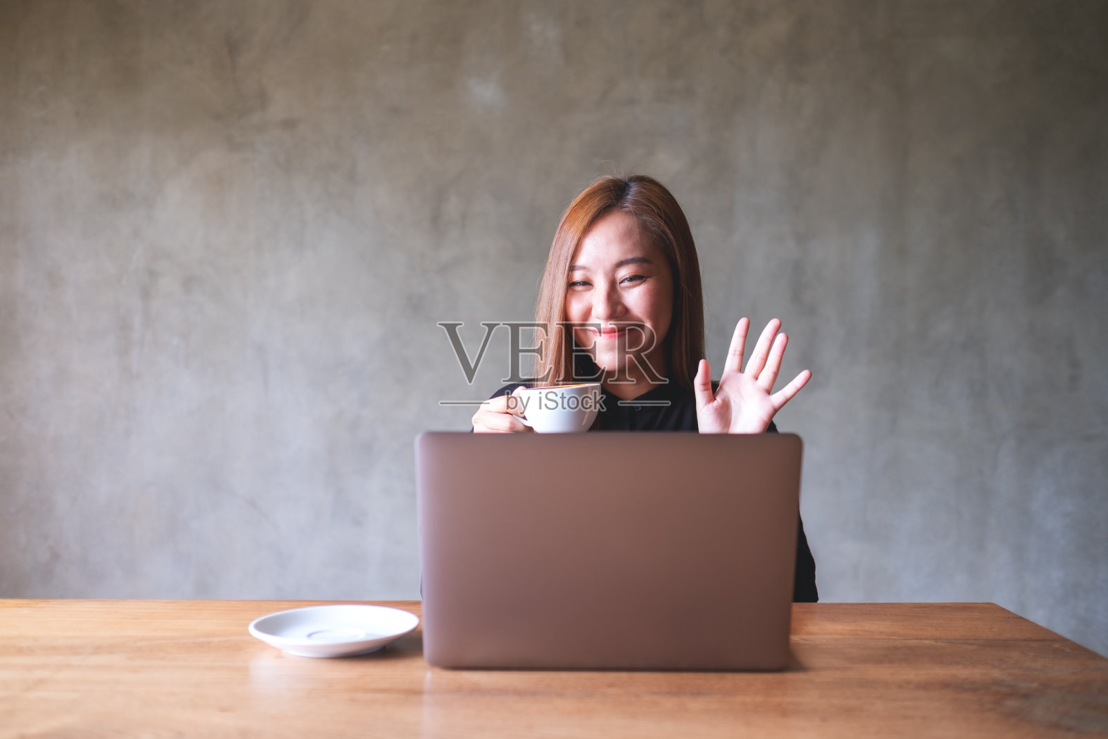 一位年轻貌美的亚洲女子一边喝咖啡,一边用笔记本电脑进行视频通话、在线会议照片摄影图片