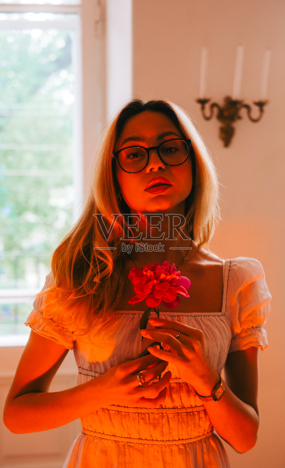 迷人的白衣年轻女子的肖像站在明亮的客厅,拿着粉红色的花。照片摄影图片