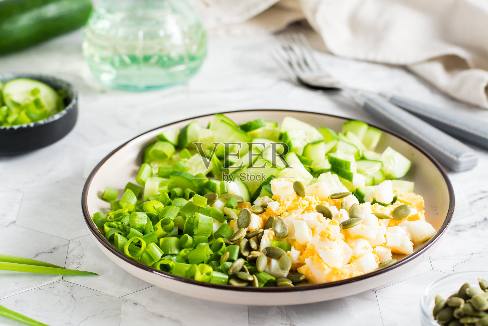 新鲜的黄瓜沙拉,煮鸡蛋和青葱在桌子上的盘子。生酮饮食。照片摄影图片