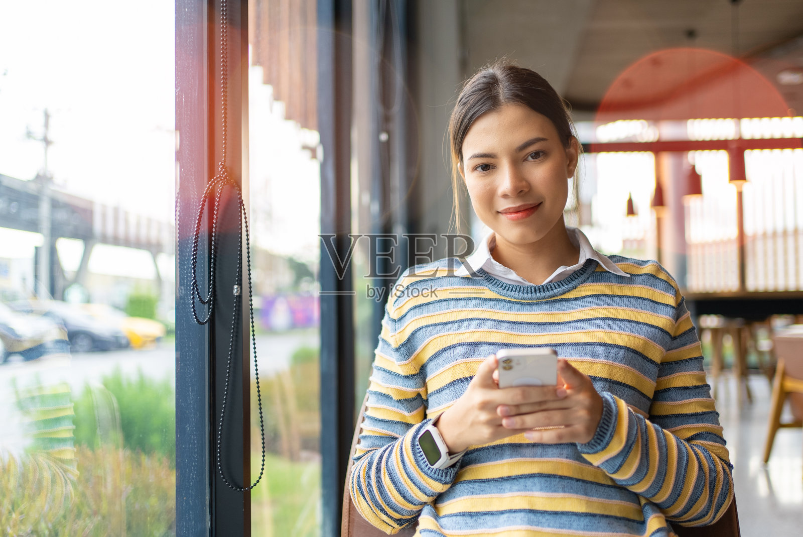 一个漂亮的女人戴着智能手表坐在咖啡店用她的智能手机输入信息。短信。照片摄影图片