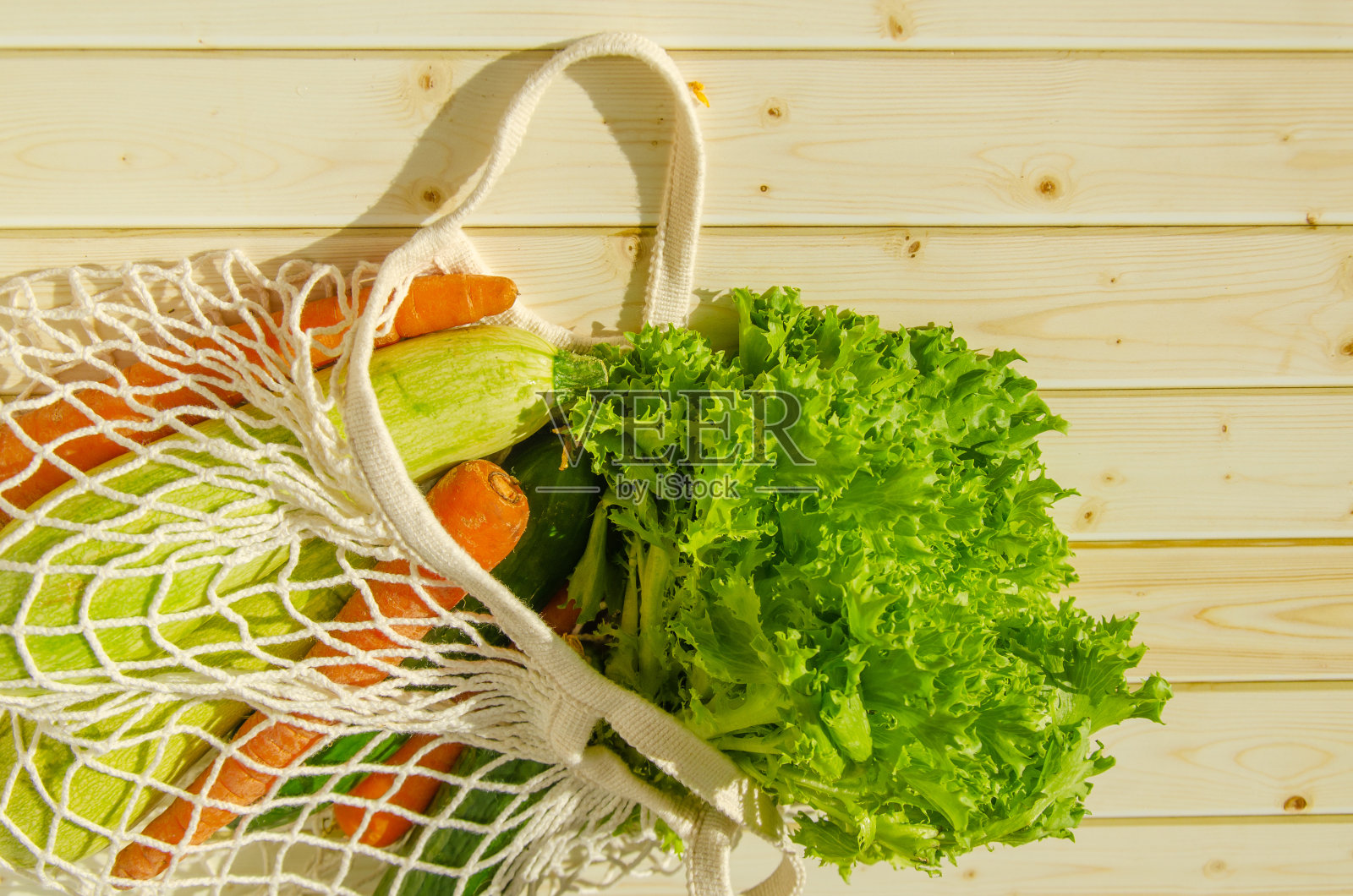 新鲜蔬菜串袋。新鲜的农场蔬菜在网袋上的木制背景。乡村照片摄影图片