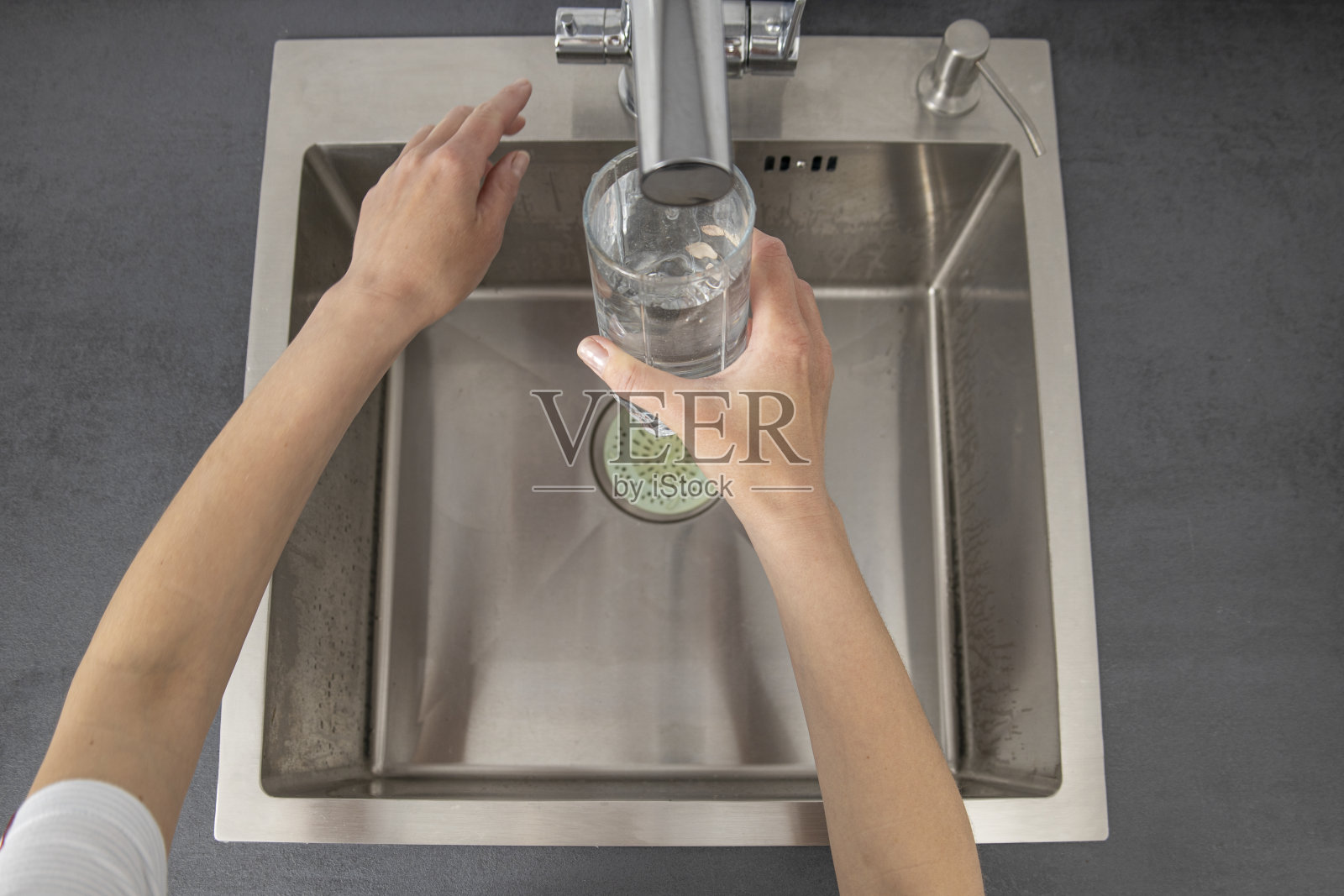 在厨房往玻璃杯里倒水的女人。俯视图,平铺照片摄影图片