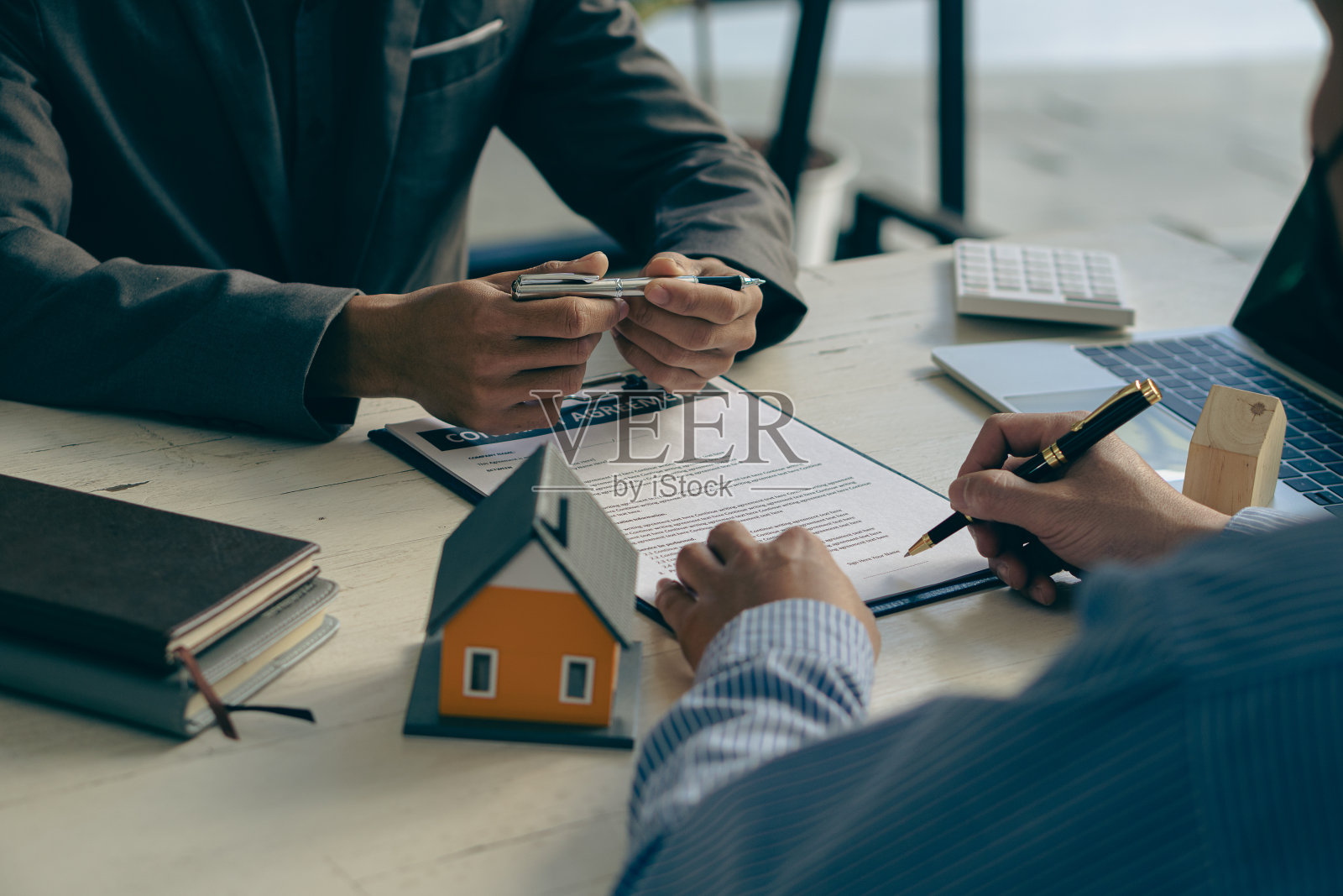 房地产经纪人讨论购房合同的条款,并要求客户签署文件,以合法地签订合同。在办公桌上卖房子的想法照片摄影图片