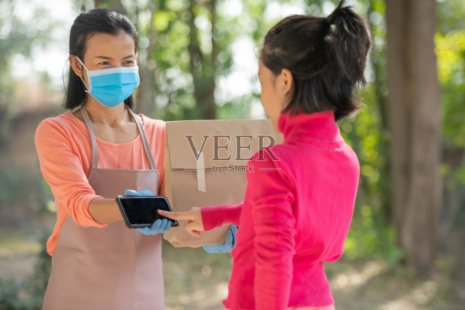 递送,邮件,人和航运的概念。年轻女子在家收到快递包裹后,用数码手机签收。在COVID-19疫情期间,快递员照片摄影图片