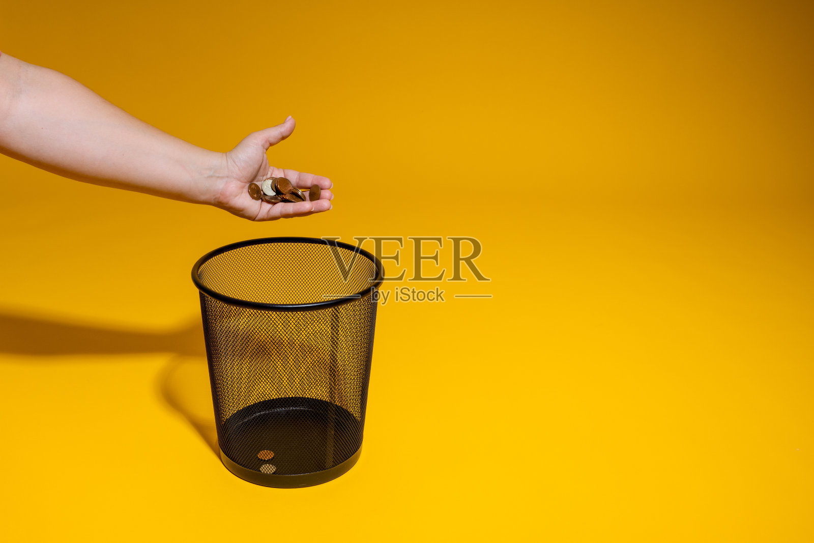 手把一把零钱扔进垃圾桶。硬币被扔进办公室的废纸篓里。价格上涨和摆脱金属货币的概念照片摄影图片