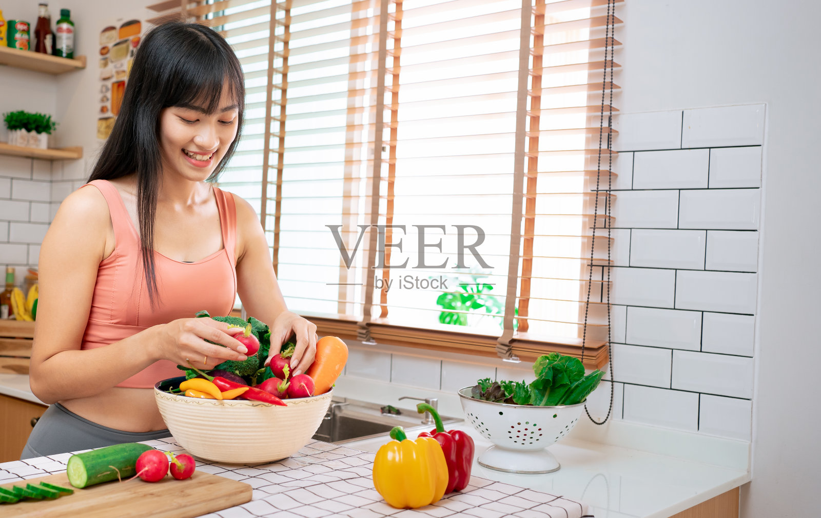 年轻的亚洲女人微笑着拿着蔬菜和水果杂货店的打击。泰国模特健身和瑜伽修身。运动穿的人在厨房吃各种有机食品。素食女性在家快乐。照片摄影图片
