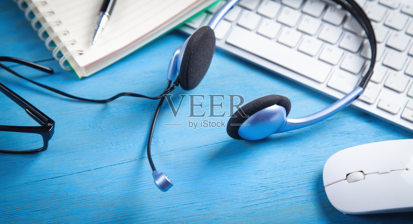 蓝色背景的客户服务耳机、电脑键盘和业务对象。照片摄影图片