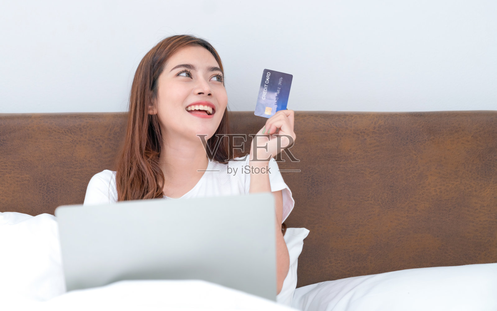 快乐的亚洲女人在家里网购,女人在家里的床上用信用卡和笔记本电脑网购照片摄影图片