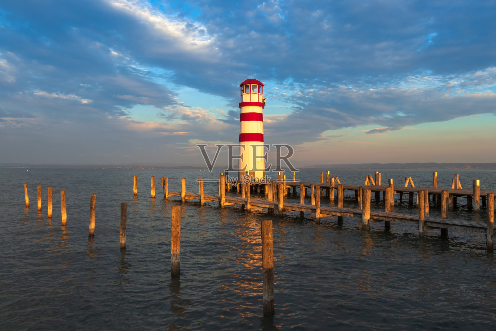 奥地利波德斯多夫的Neusiedl湖上有一座通往湖的木制码头和一座红白相间的灯塔。背景是日出时壮观的天空。照片摄影图片