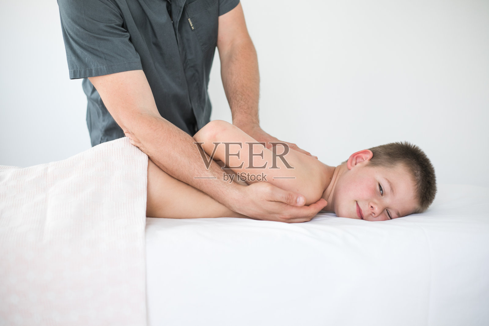 男孩蹒跚学步的放松从治疗按摩。在临床中与病人一起治疗儿童背部的理疗师照片摄影图片