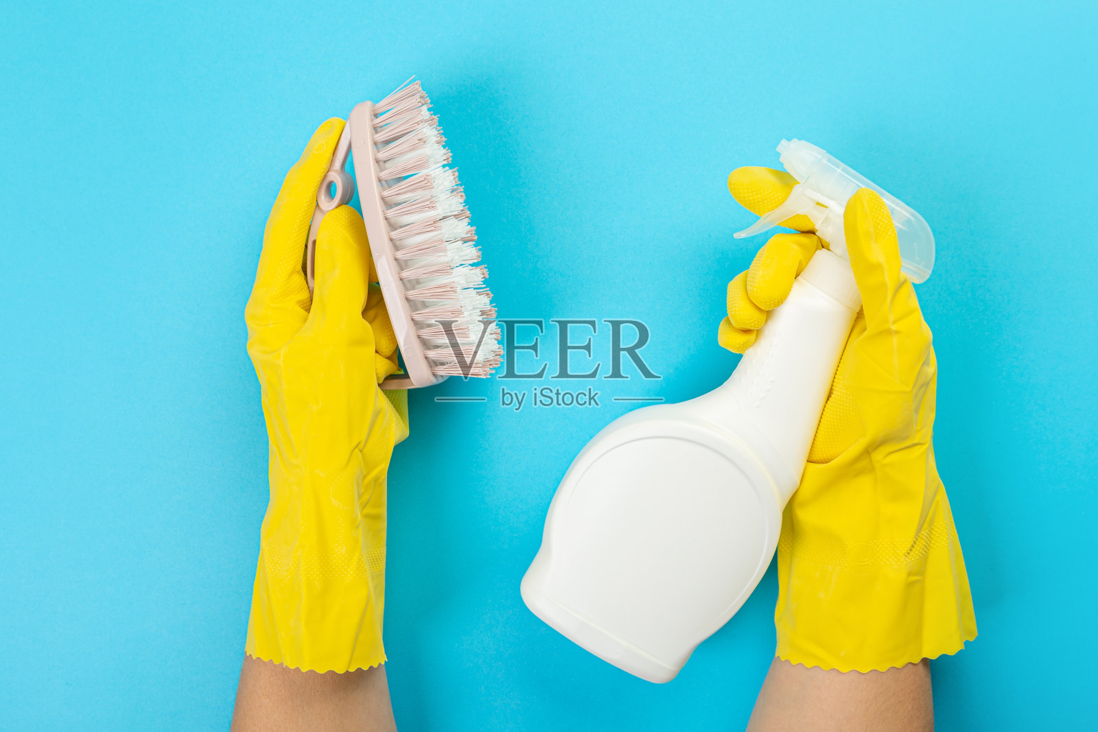 戴着黄色橡胶防护手套的家庭主妇手里拿着一瓶家用化学品和一块抹布。厨房、浴室和其他房间各种表面的清洁剂。浅粉彩蓝色背景。照片摄影图片