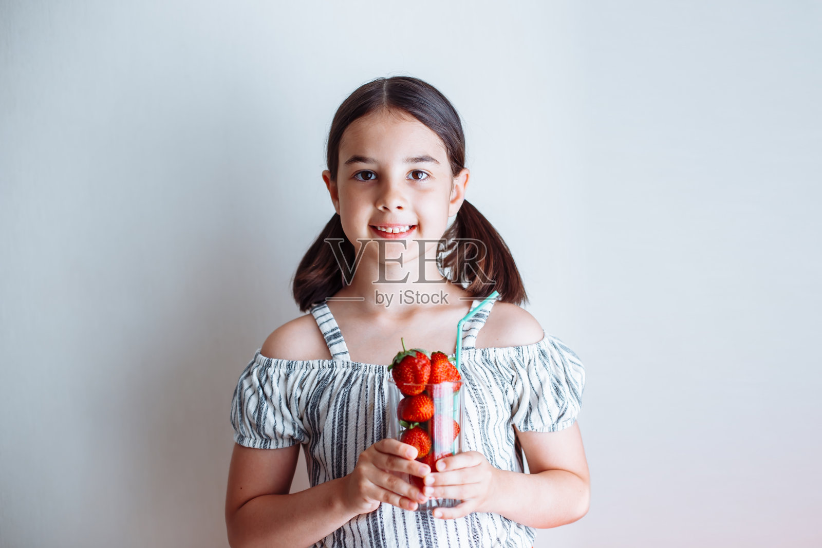 一个可爱的黑发小女孩,拿着一个盛着新鲜草莓的杯子照片摄影图片