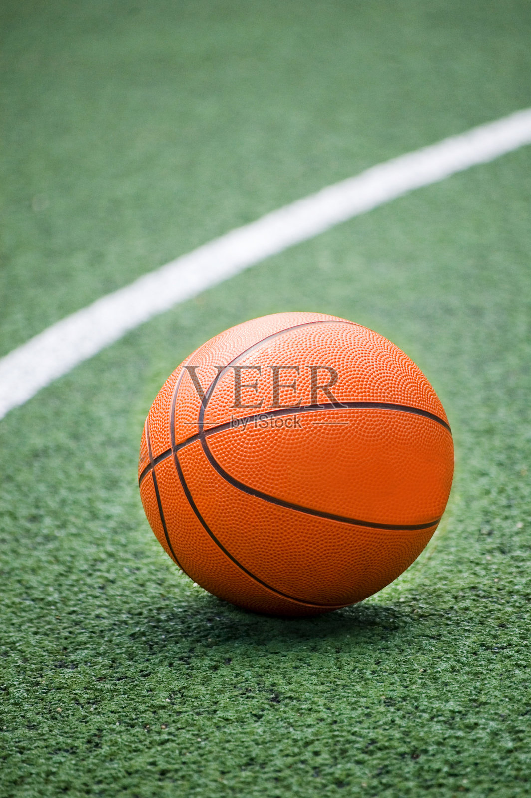 橙色的篮球躺在绿色的操场上。照片摄影图片