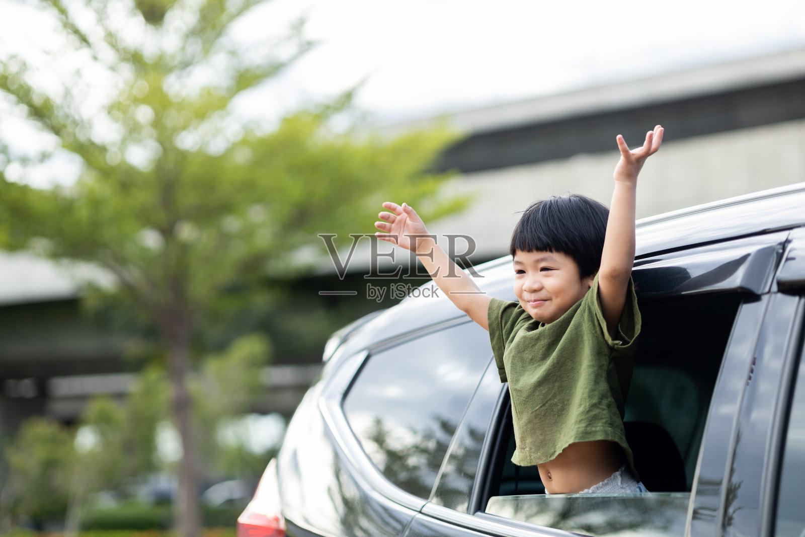 快乐的亚洲男孩在与他的家人旅行期间向车窗外挥手示意你好。一个小孩把头伸出挡风玻璃,在暑假里开车旅行。照片摄影图片