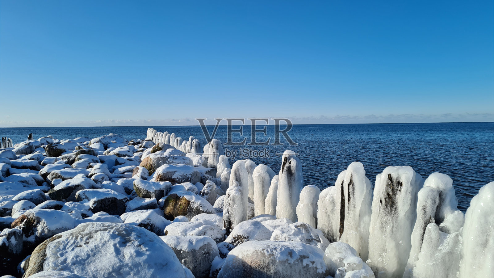 冬天阳光明媚的日子里,海边结冰的木杆,碧水蓝天。照片摄影图片