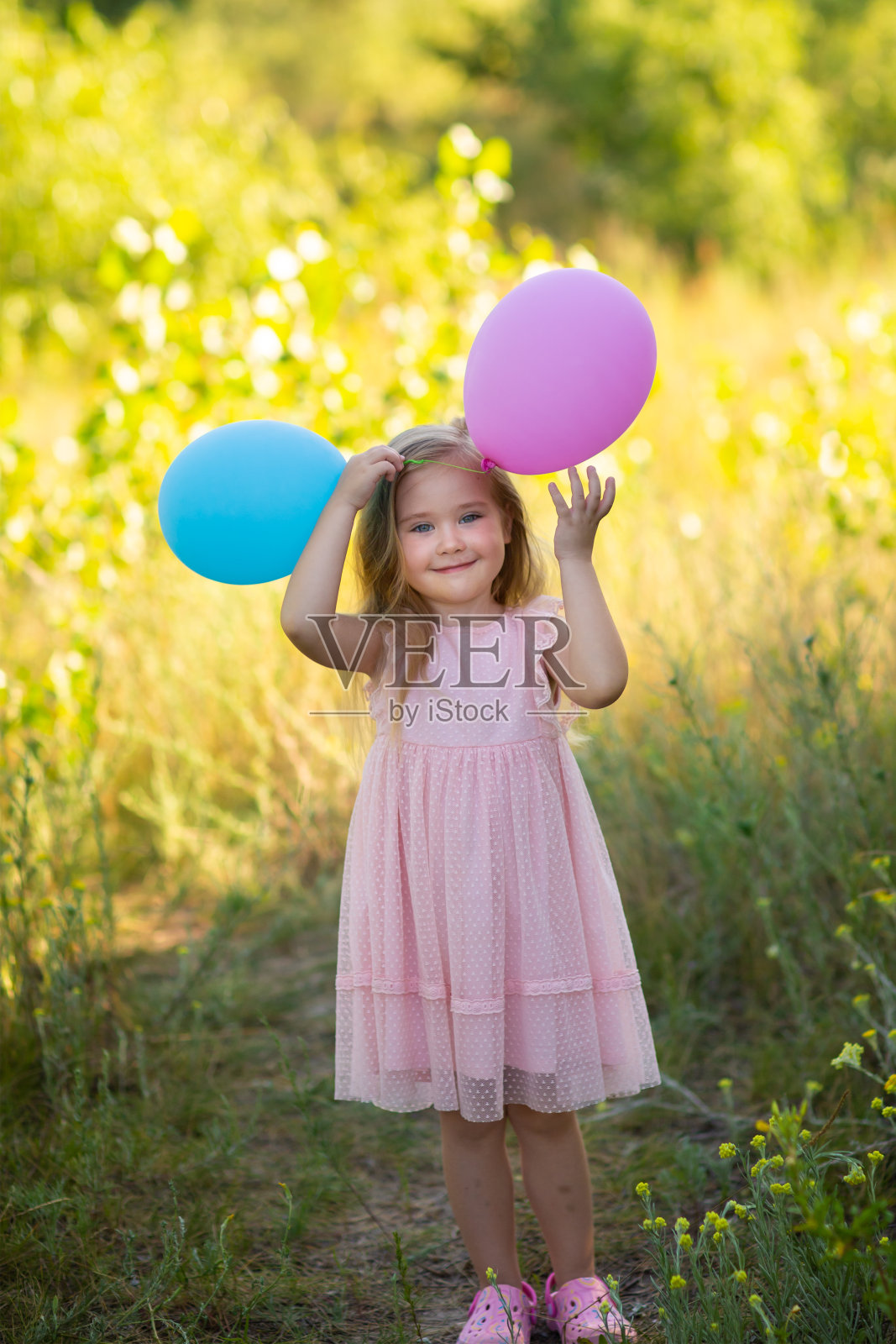一个穿着粉红色裙子的女孩站在夏天的草地上,手里拿着气球照片摄影图片
